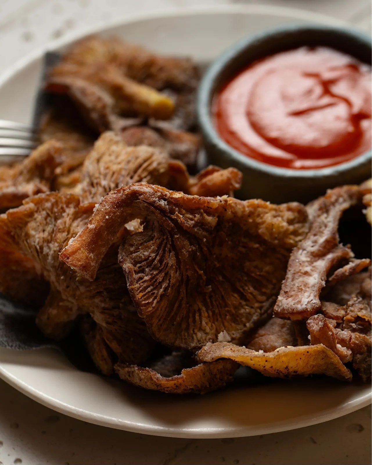 Crispy fried oyster mushrooms on a white plate with a bowl of beetroot ketchup