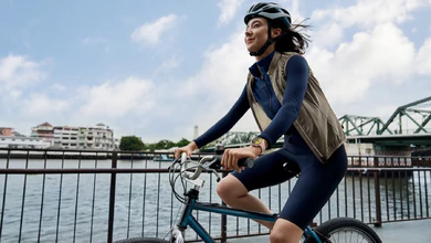 A cyclist wearing the gold HUAWEI WATCH 6 rides along a river promenade.