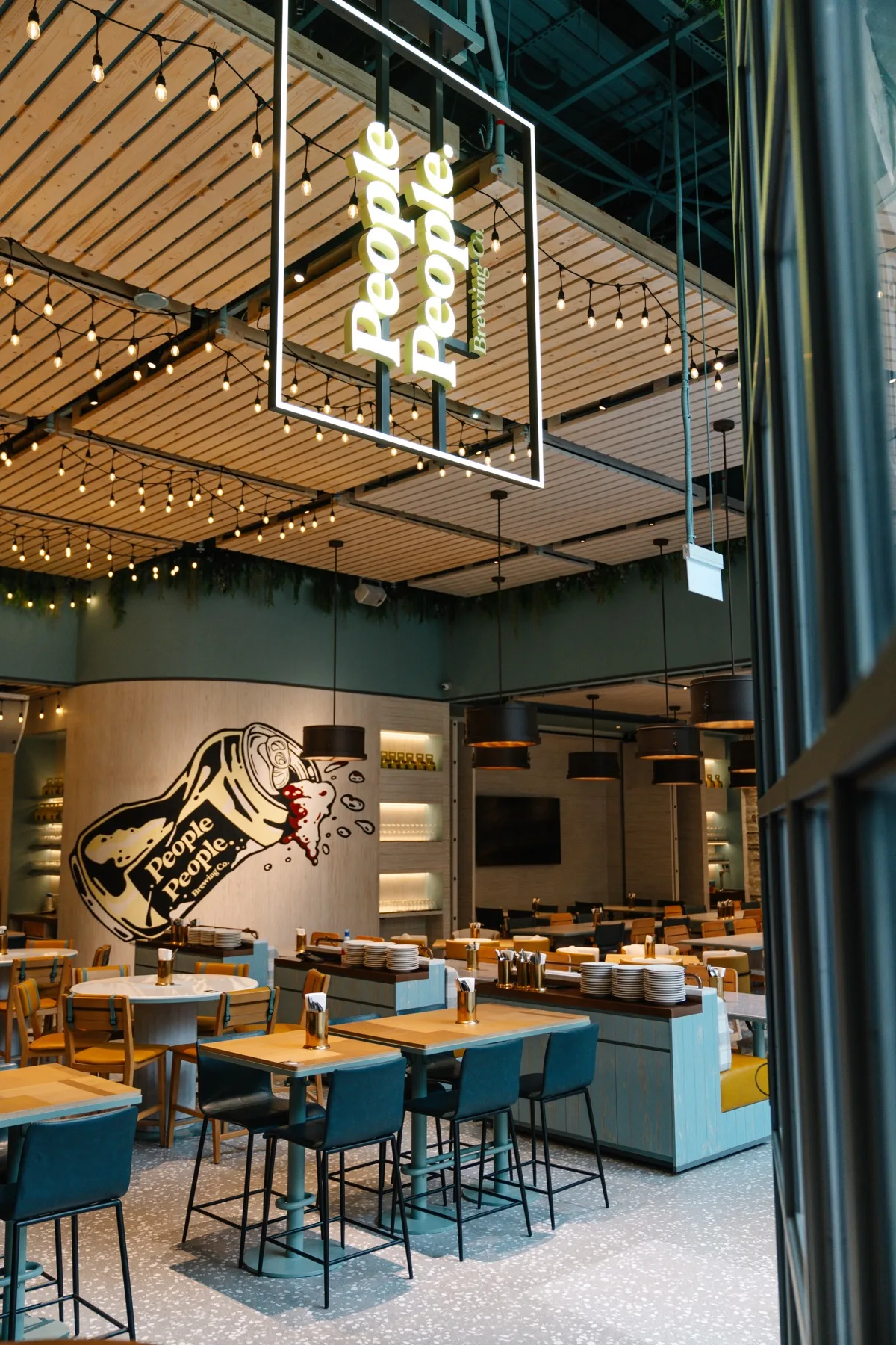 The dining room at People People Brewing Co. with string lights, a can mural and tables