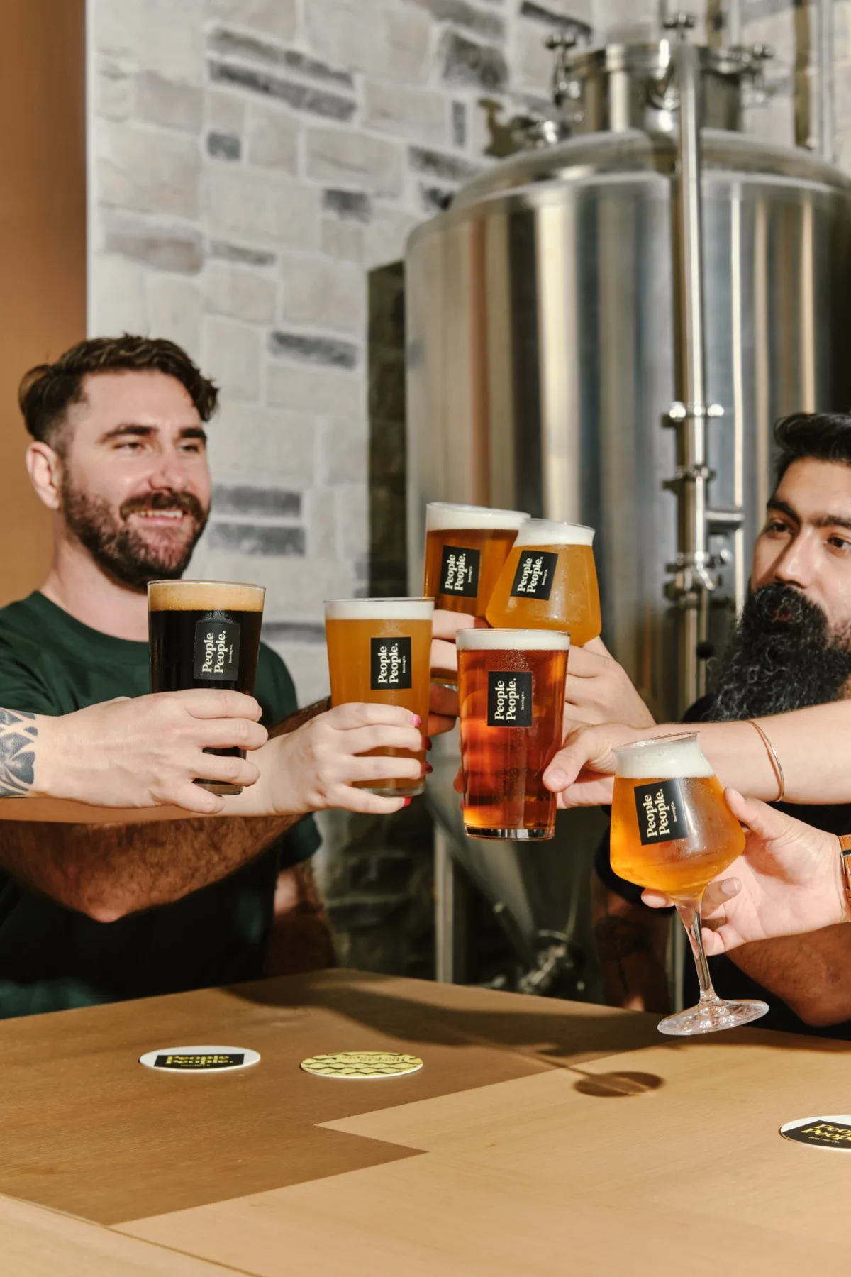 Guests toasting with glasses of People People draft beer in front of a stainless steel brew tank