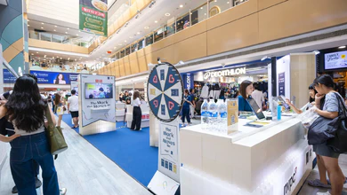 Visitors gather around a Spin & Win wheel and a display at the COG10 Travelling Showcase booth in a mall atrium