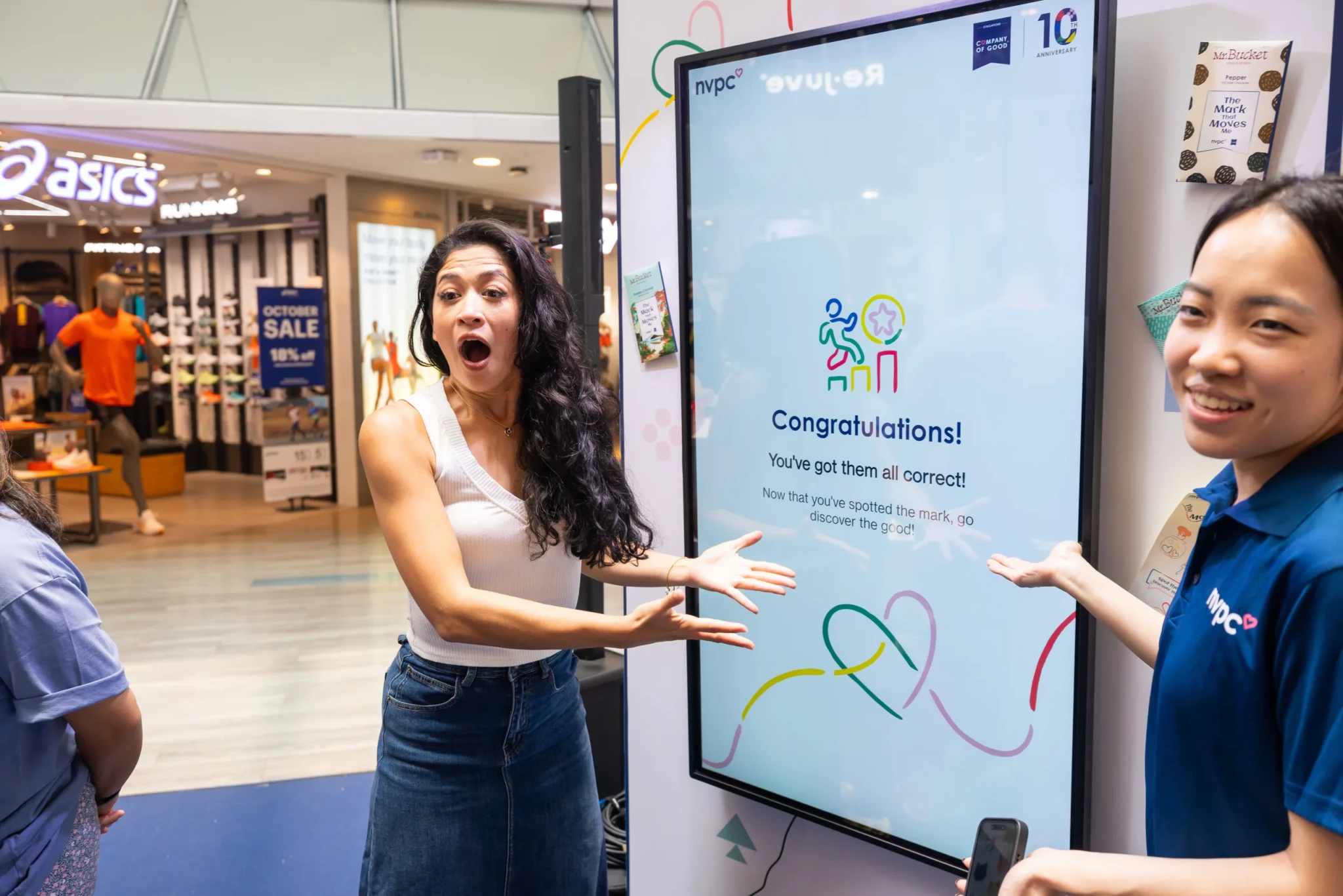 A visitor reacts with surprise beside an interactive screen as a staff member points to a congratulations message