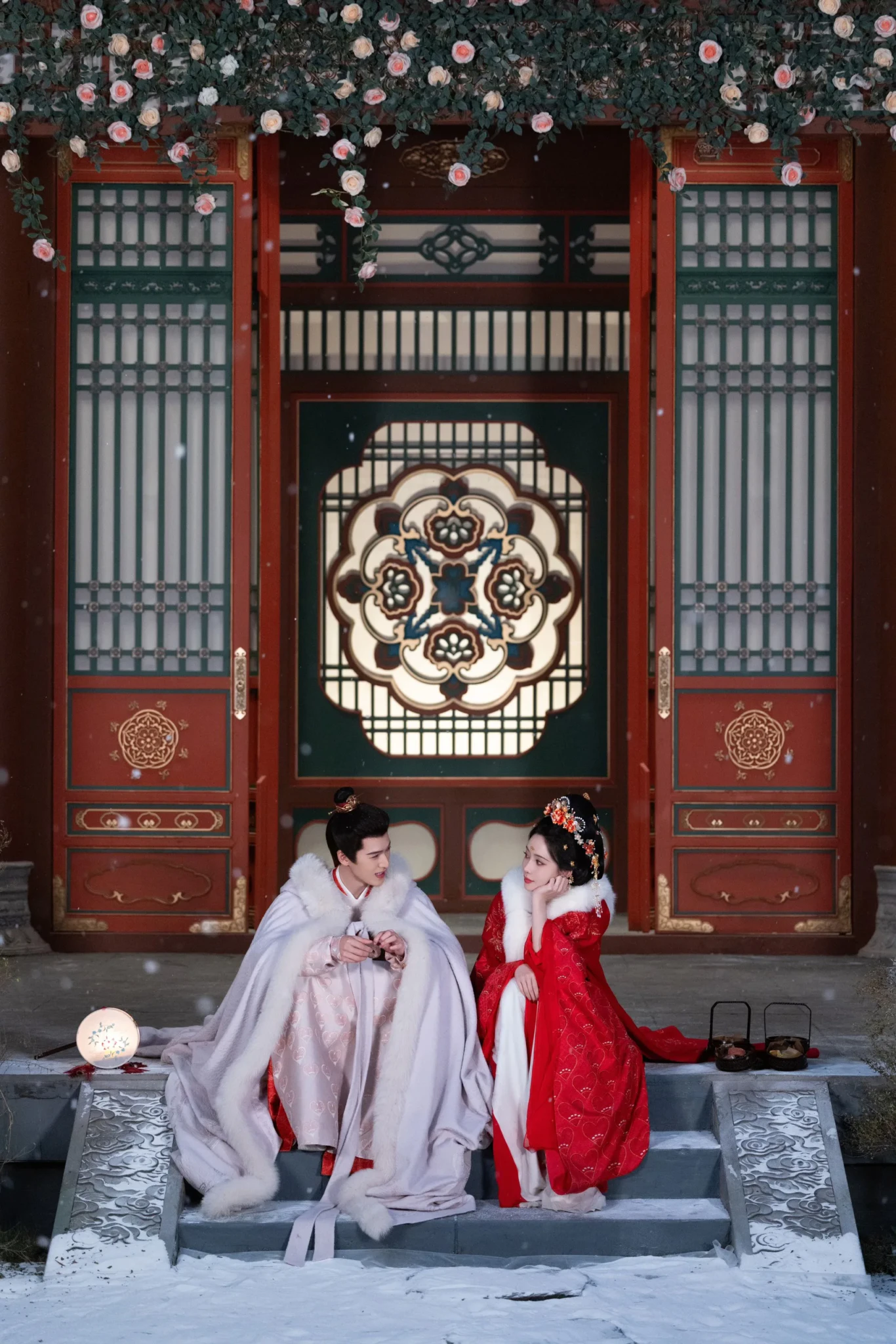 Meng Ziyi and Li Yunrui in hanfu sitting on snowy steps in front of a red lattice doorway