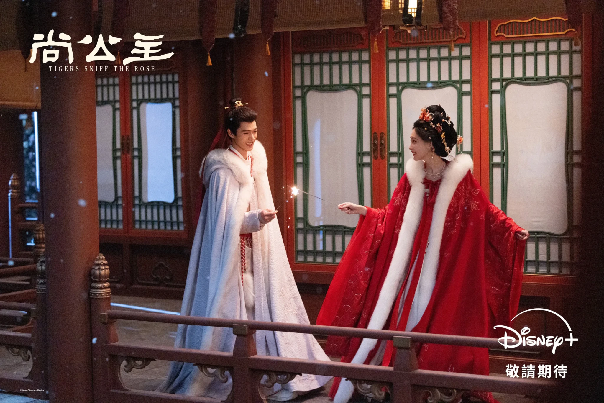 Key art for Tigers Sniff the Rose showing two leads in white and red fur-trimmed capes sharing a sparkler on a snowy balcony