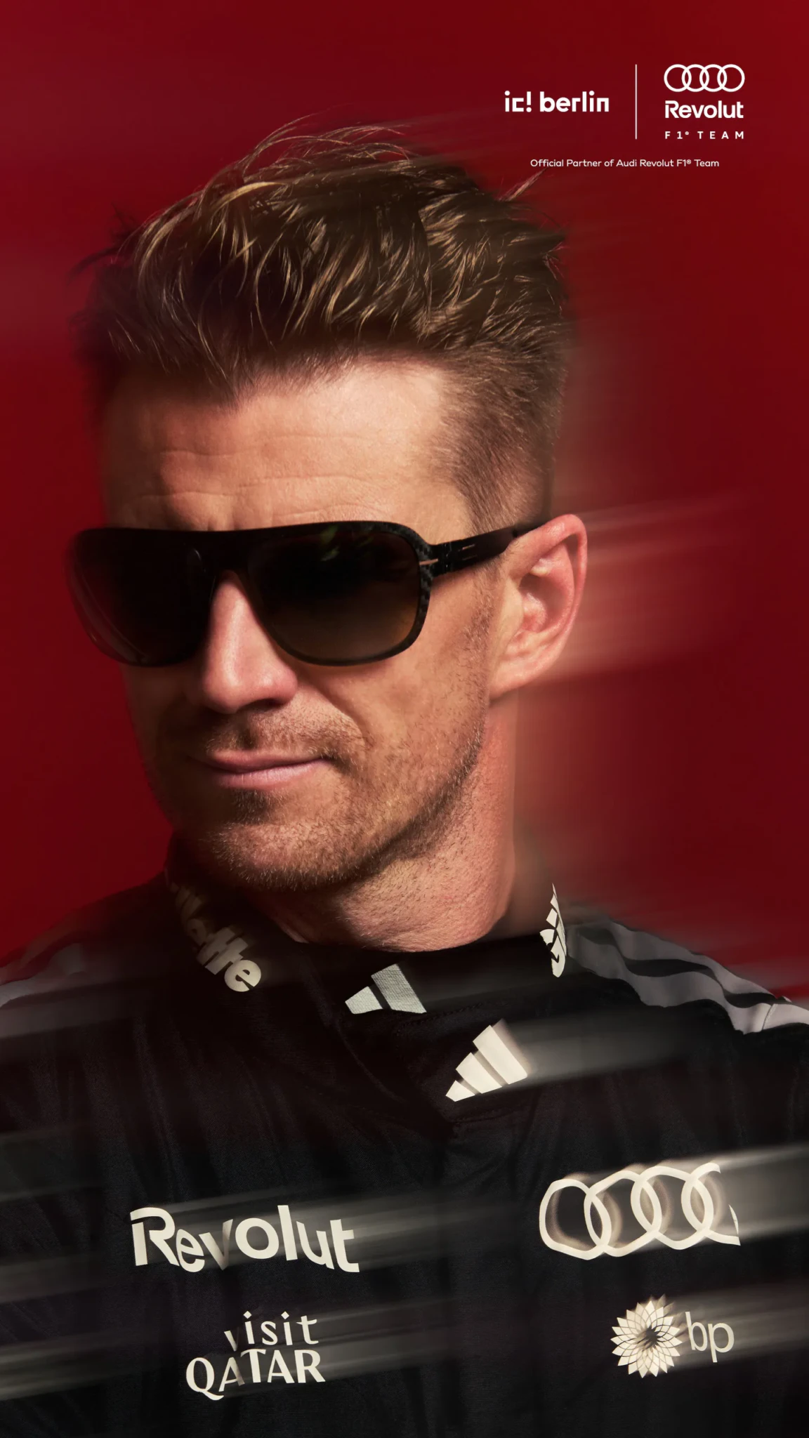 A man in dark tinted sunglasses and a black Audi Revolut F1 Team jacket with sponsor logos