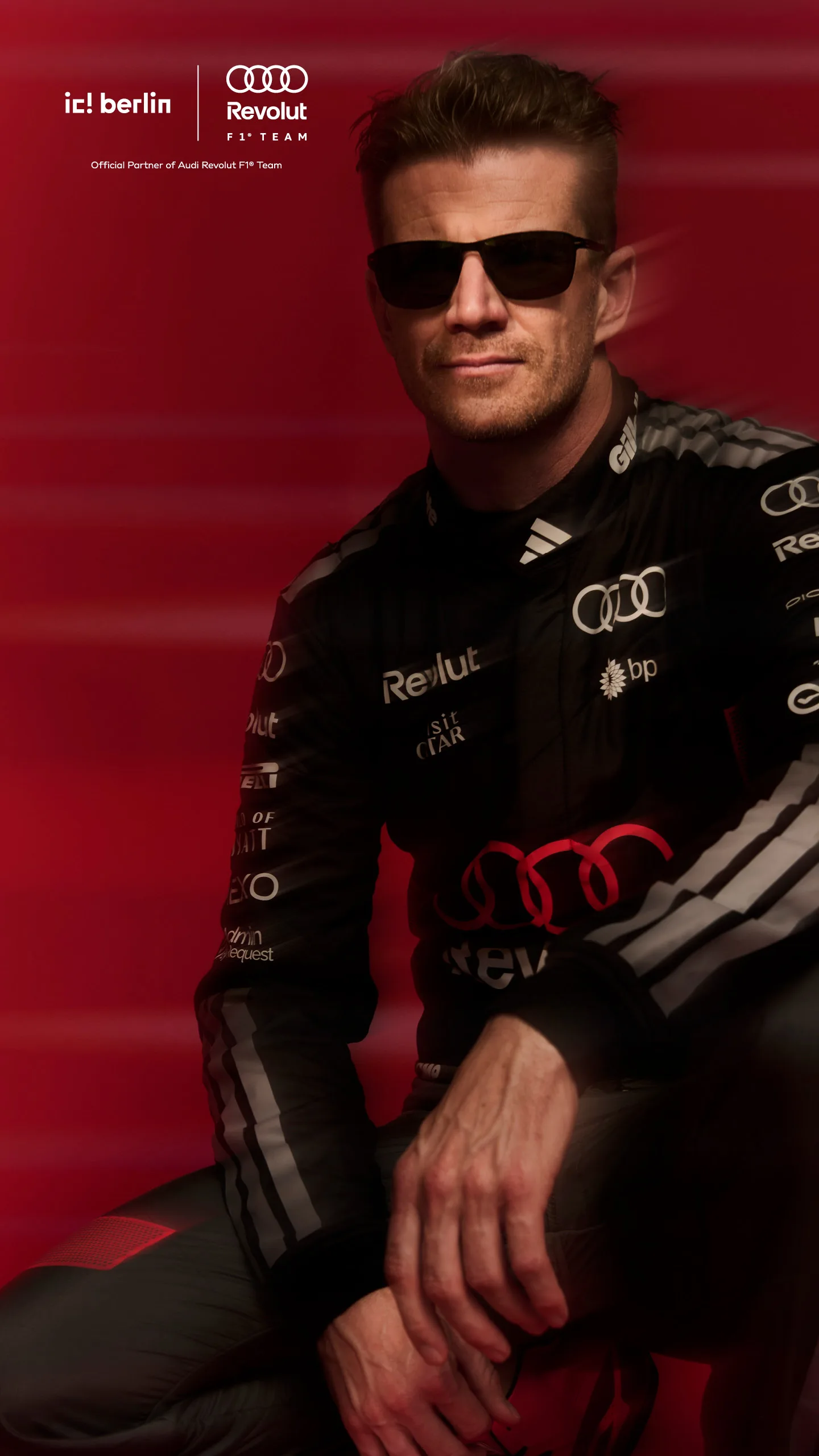 Driver in black Audi Revolut F1 Team suit and sunglasses seated against a red background, ic! berlin campaign