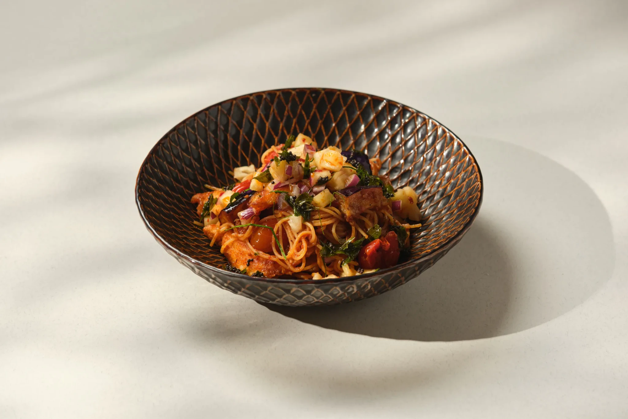 Snapper Assam Arrabbiata pasta at PS.Cafe Harding, topped with diced vegetables, herbs and cherry tomatoes in a dark ceramic bowl