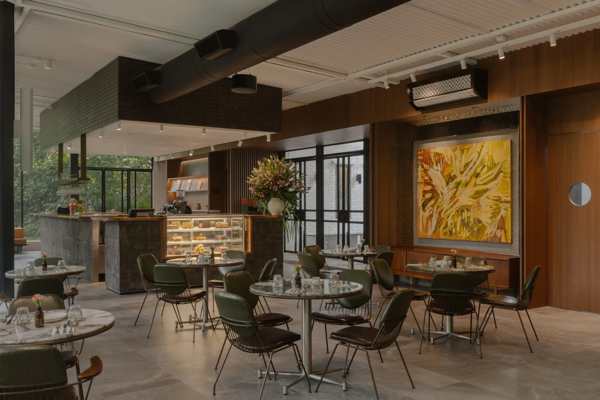 Interior of PS.Cafe Harding with marble tables, green wire chairs, bakery counter and large yellow painting