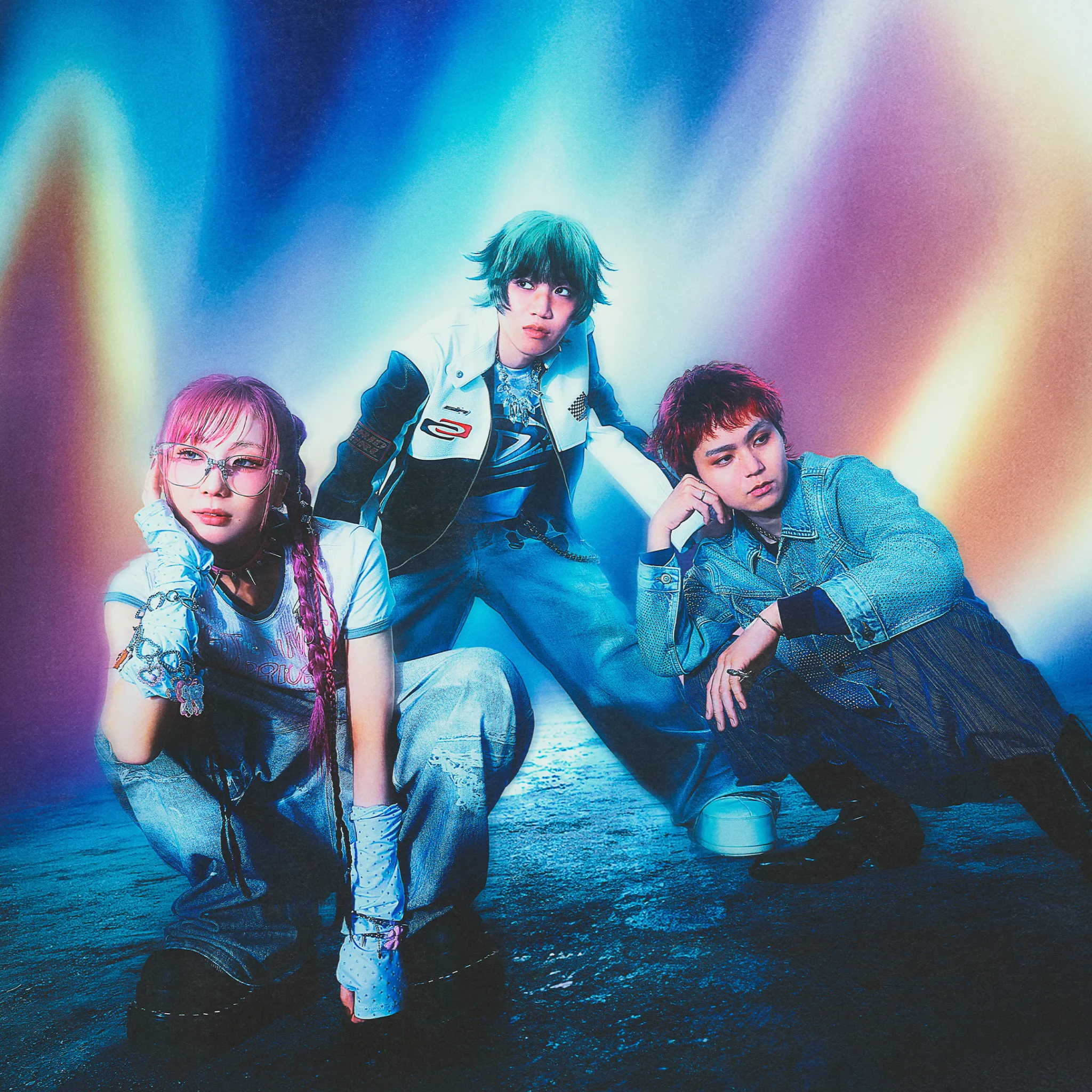 Three members of the band muque crouch and pose in front of a glowing blue, pink and yellow light backdrop, wearing denim and layered streetwear.