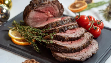 Sliced roasted beef ribeye with thyme and cherry tomatoes on a slate board