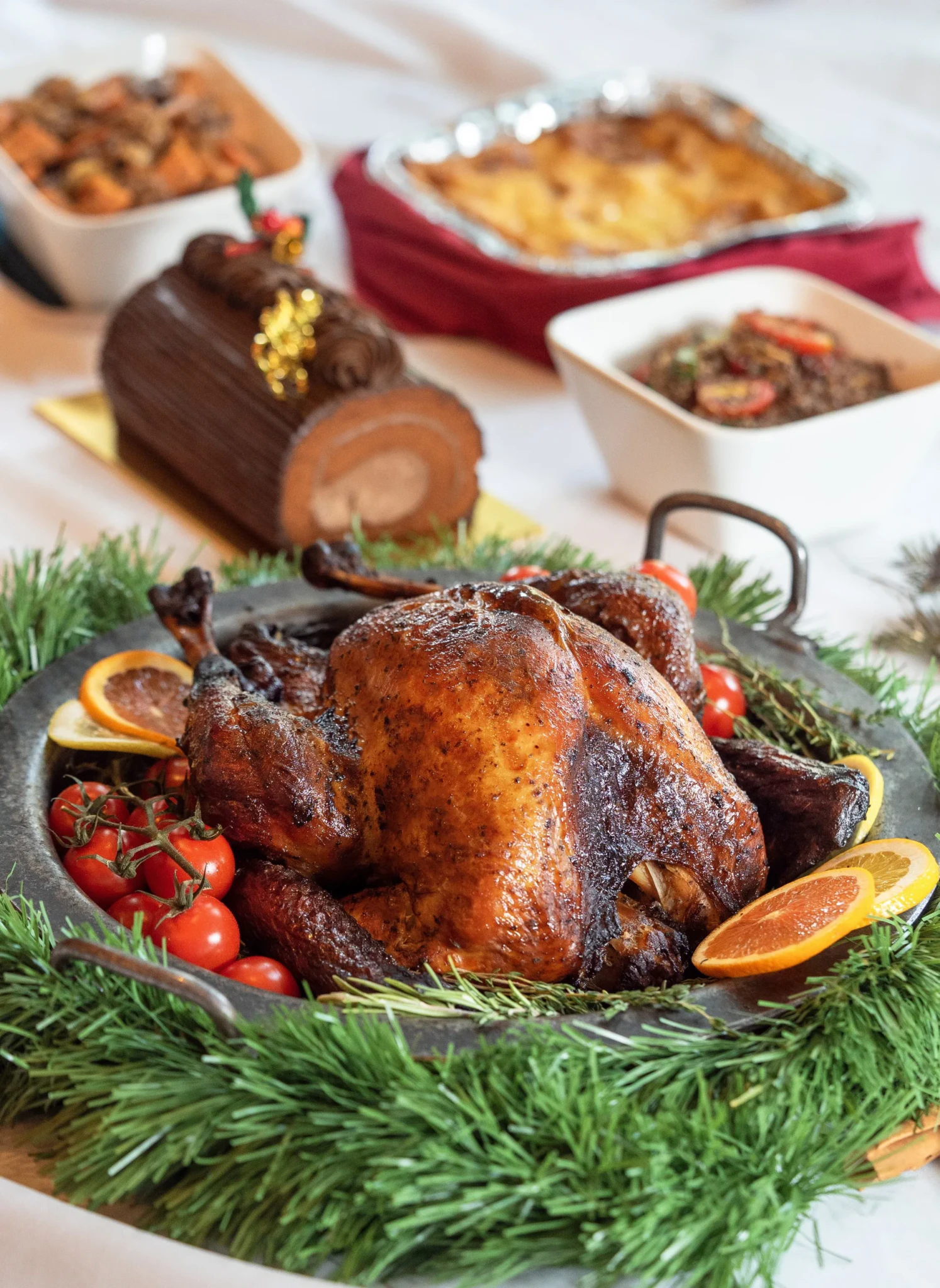 A glazed roast with festive sides and a Yule Log cake on a dining table