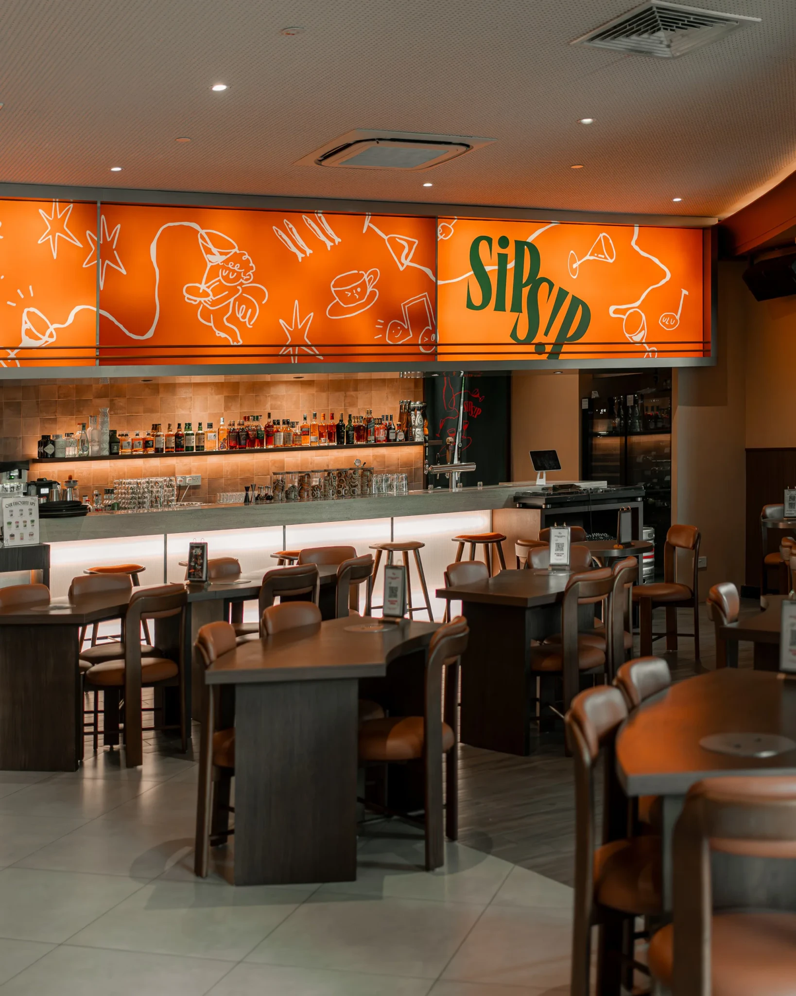 The interior of Sip Sip, with an orange hand-drawn mural and a SIPSIP sign above a bar lined with spirit bottles