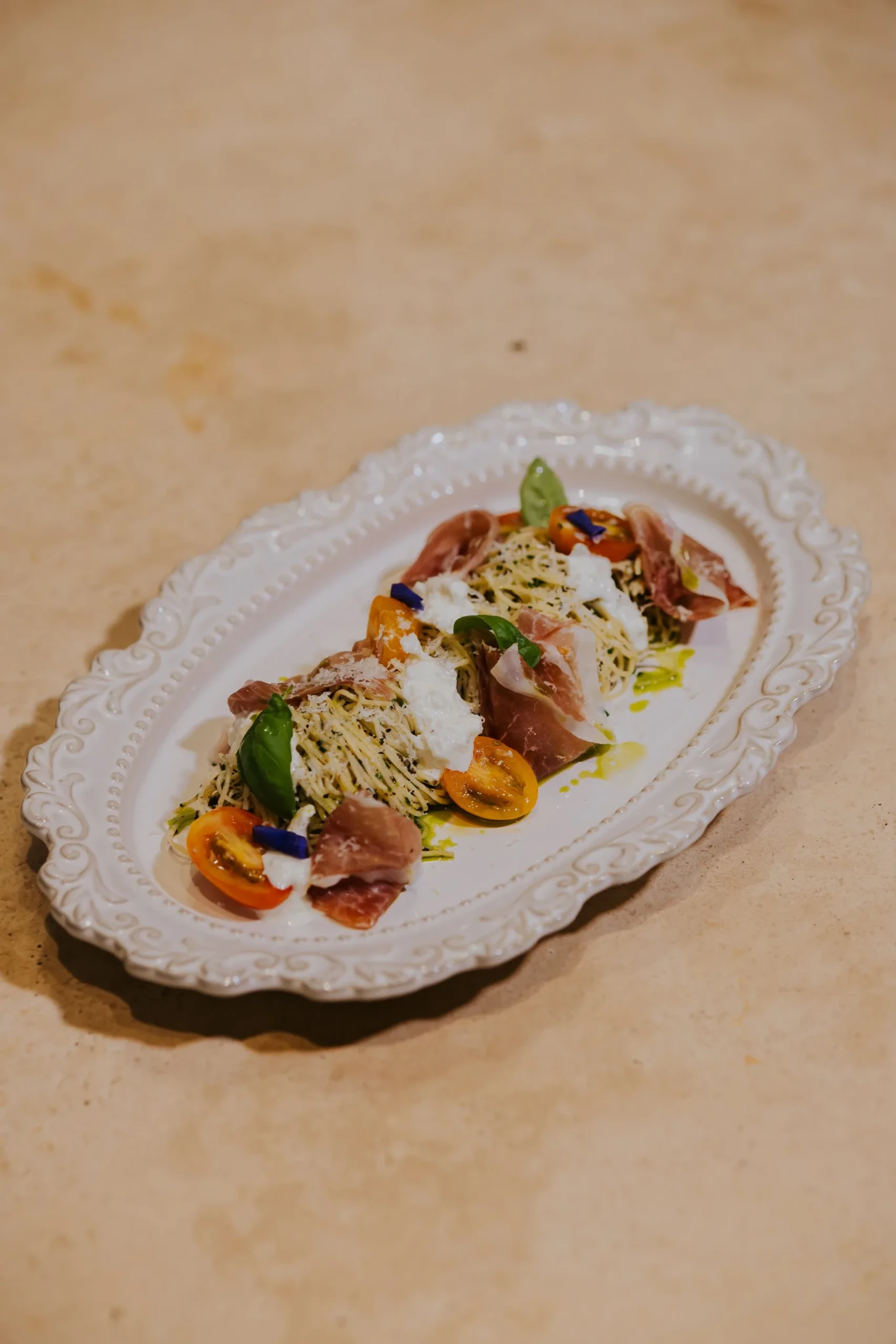 A plate of capellini topped with burrata, prosciutto, halved cherry tomatoes and basil