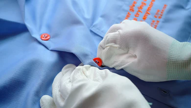 White-gloved hands fastening an orange button on a blue shirt printed with encouraging slogans