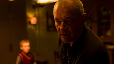 Jean-Pierre Jeunet in a dimly lit interior with a young boy in a red sweater blurred behind him