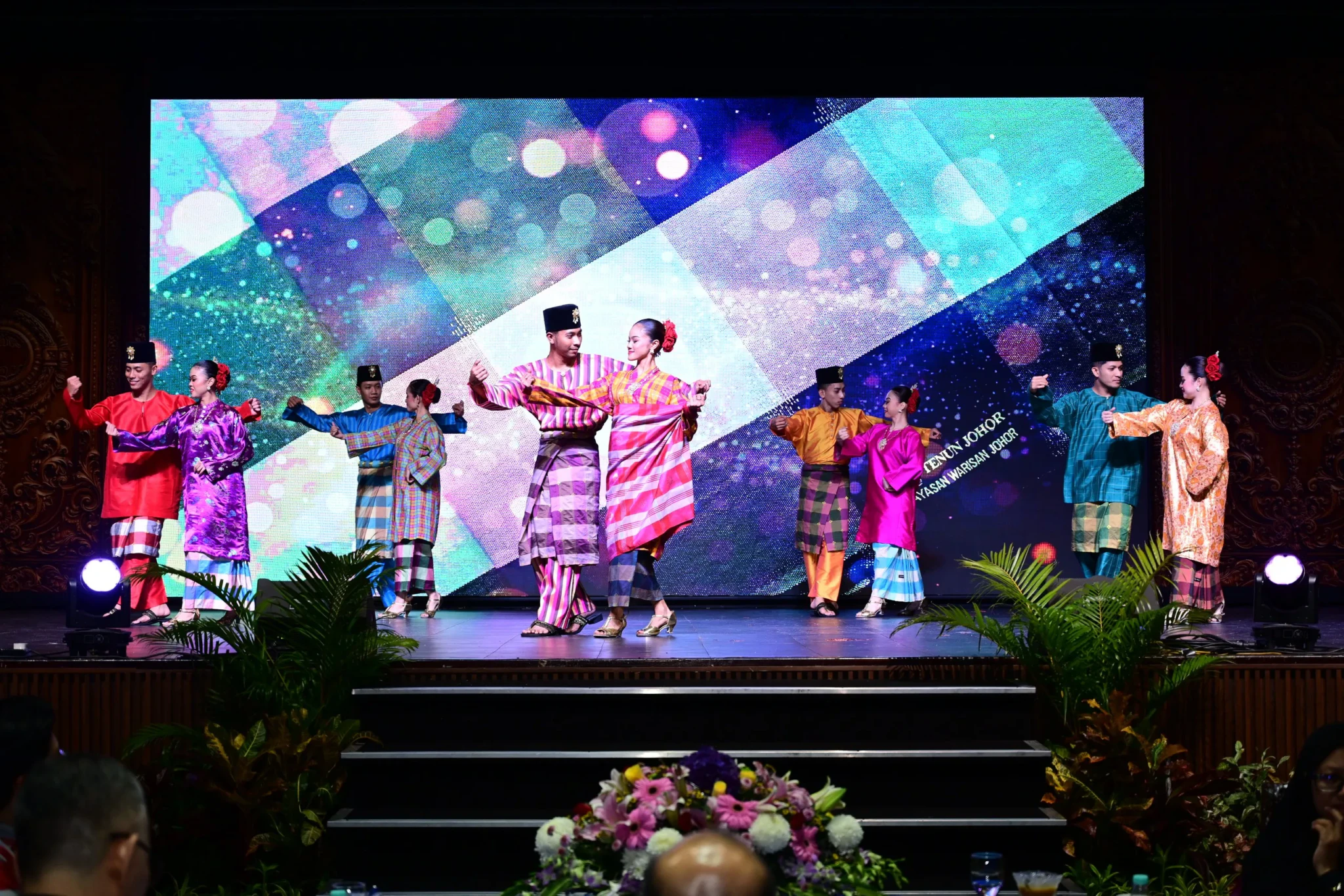 Dancers in colourful traditional Malay costumes performing on stage before a glowing LED backdrop