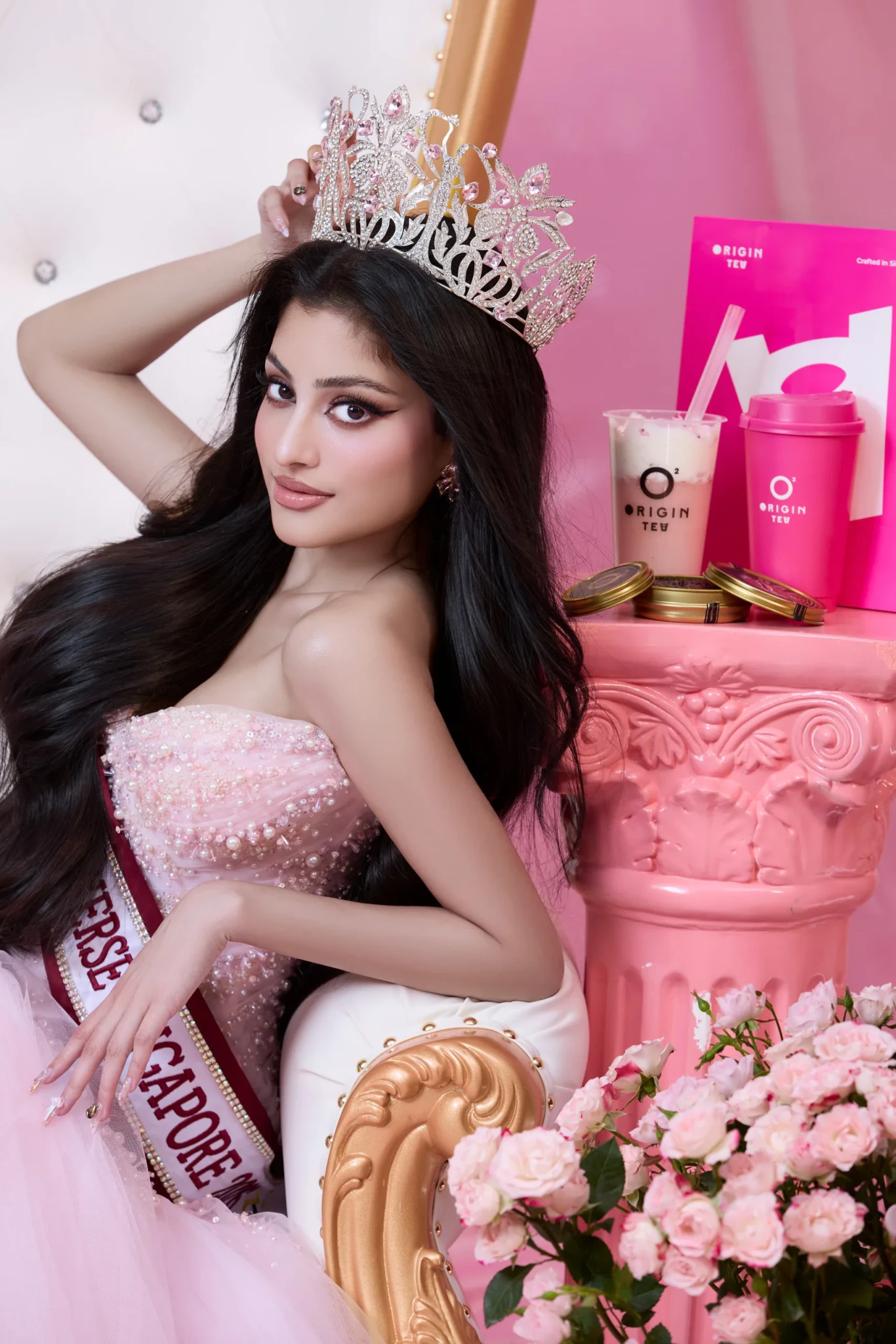 Riona Dighe in a pink gown and tiara seated beside pink Origin Tea cups and roses