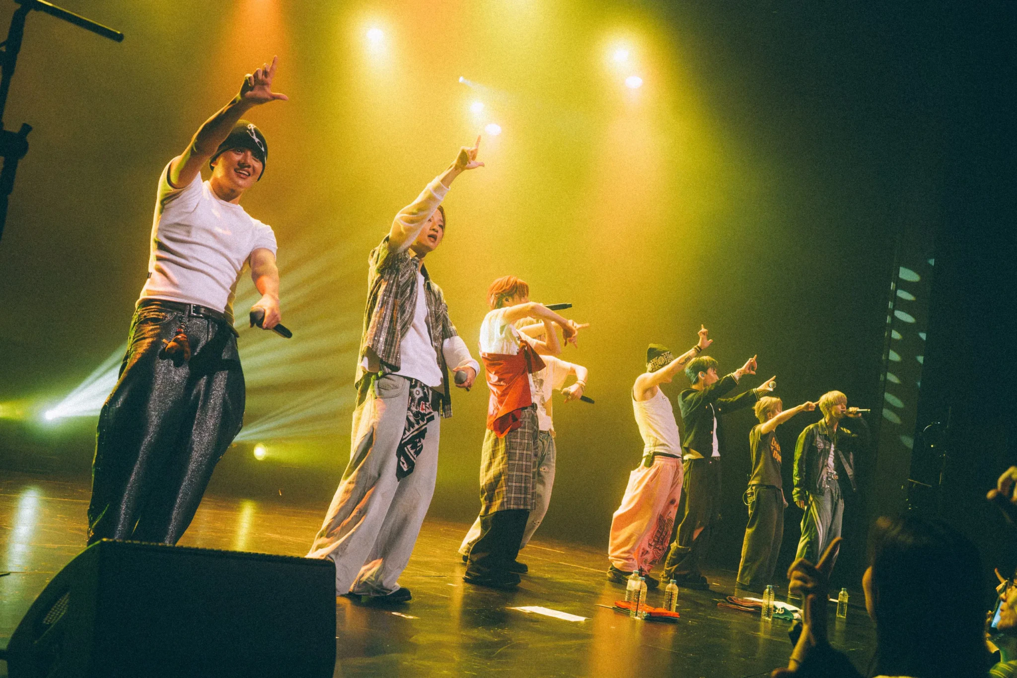ONE OR EIGHT point to the crowd from the front of the stage under yellow-green lights at Victoria Theatre