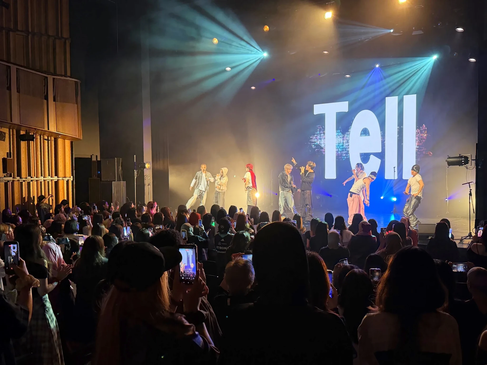 YUGA raises a hand as REIA and their ONE OR EIGHT bandmates perform with a word projected on the screen behind them