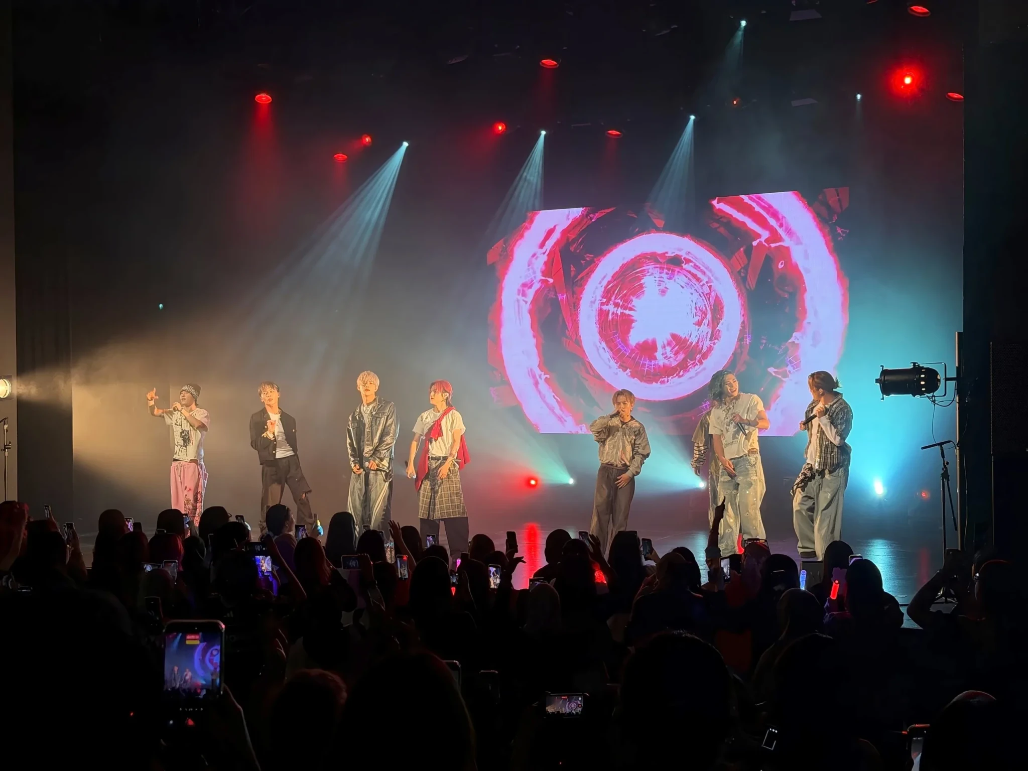YUGA, REIA and their ONE OR EIGHT bandmates perform beneath a red ring on the rear screen while audience members hold up lightsticks