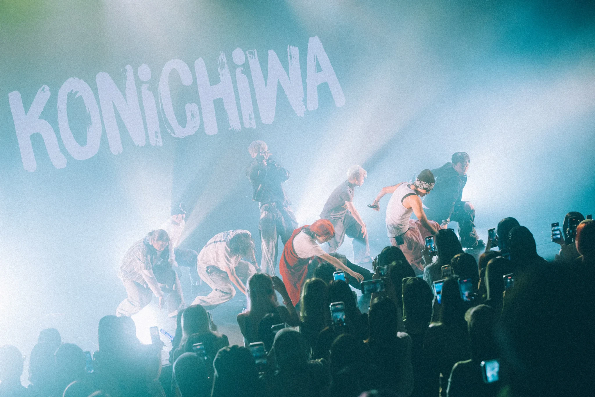 ONE OR EIGHT dance in blue haze beneath a KONICHIWA graphic on the rear screen as fans film on their phones