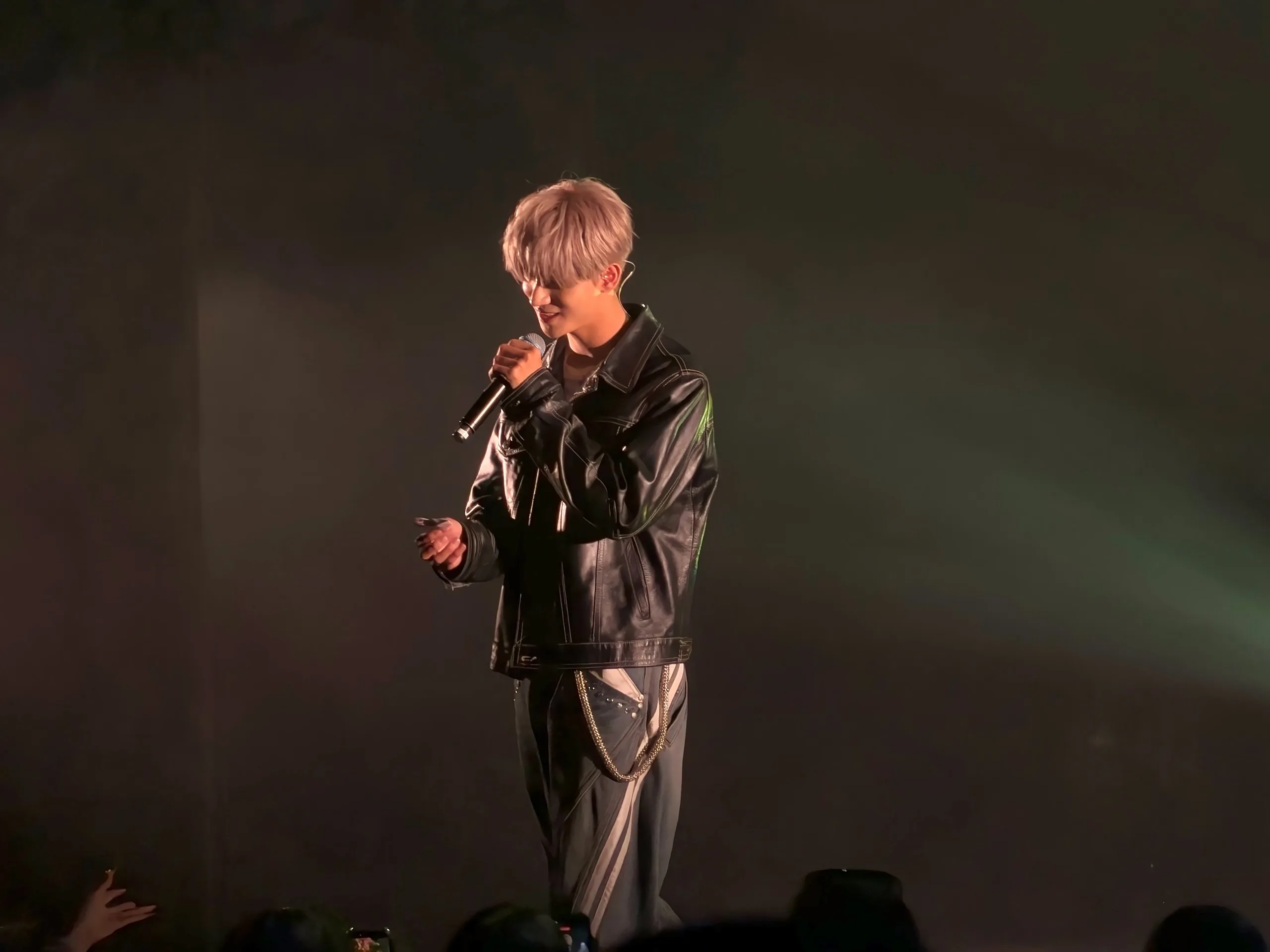 REIA of ONE OR EIGHT sings in a black leather jacket, his silver hair lit against a dark stage
