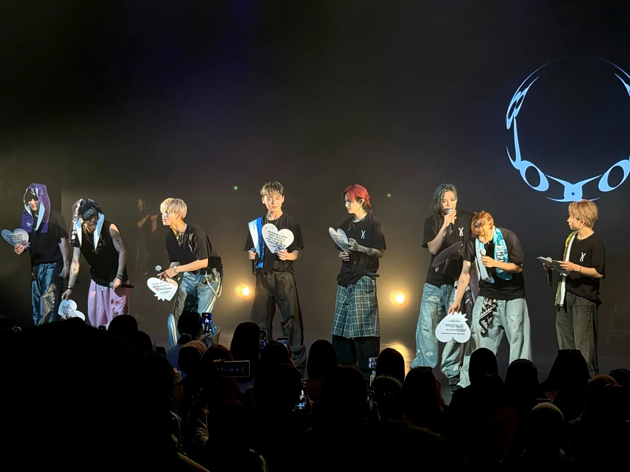 YUGA, REIA and their ONE OR EIGHT bandmates hold up white heart banners from the fans' Invincible project
