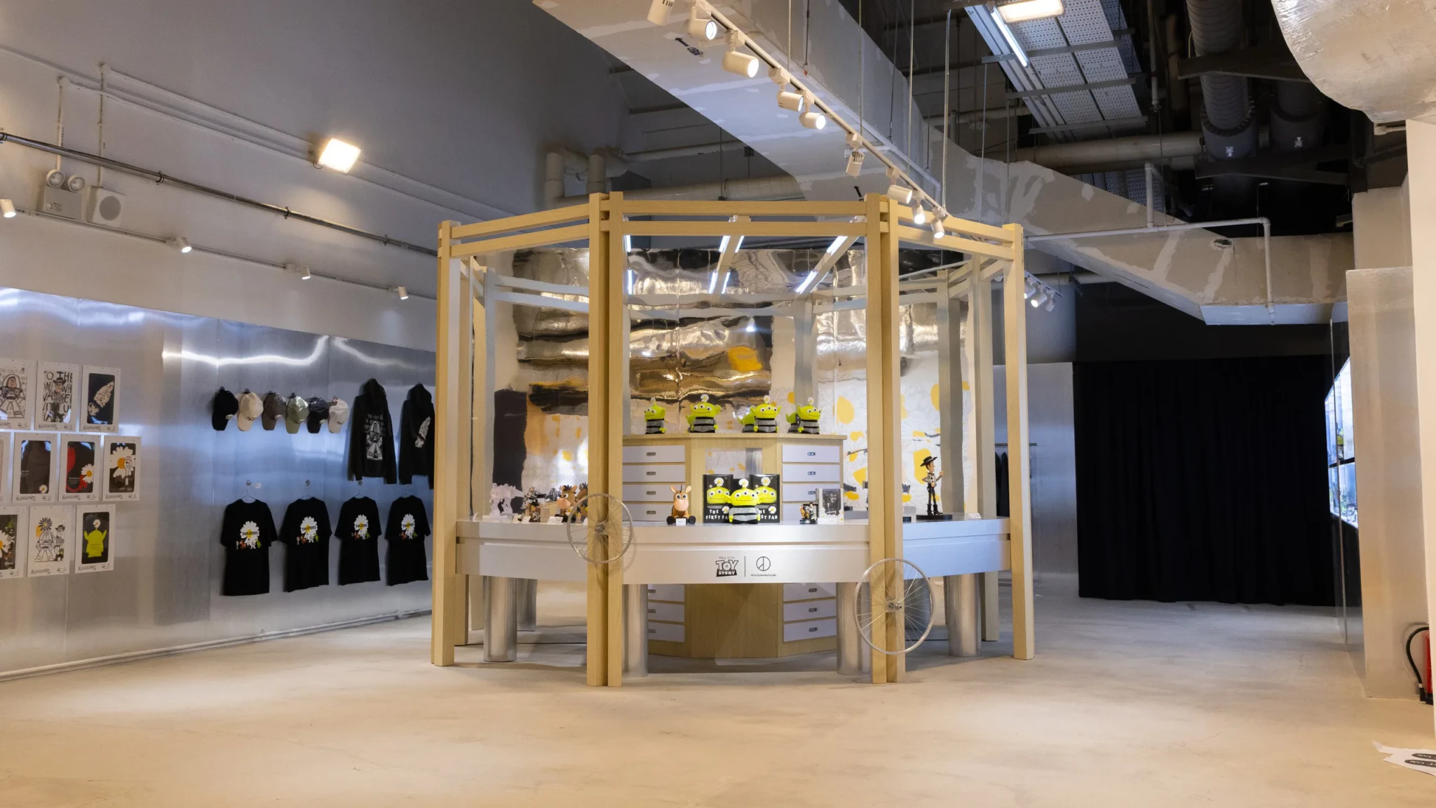 A wooden display kiosk of Toy Story collectibles with black tees hung on a metal wall