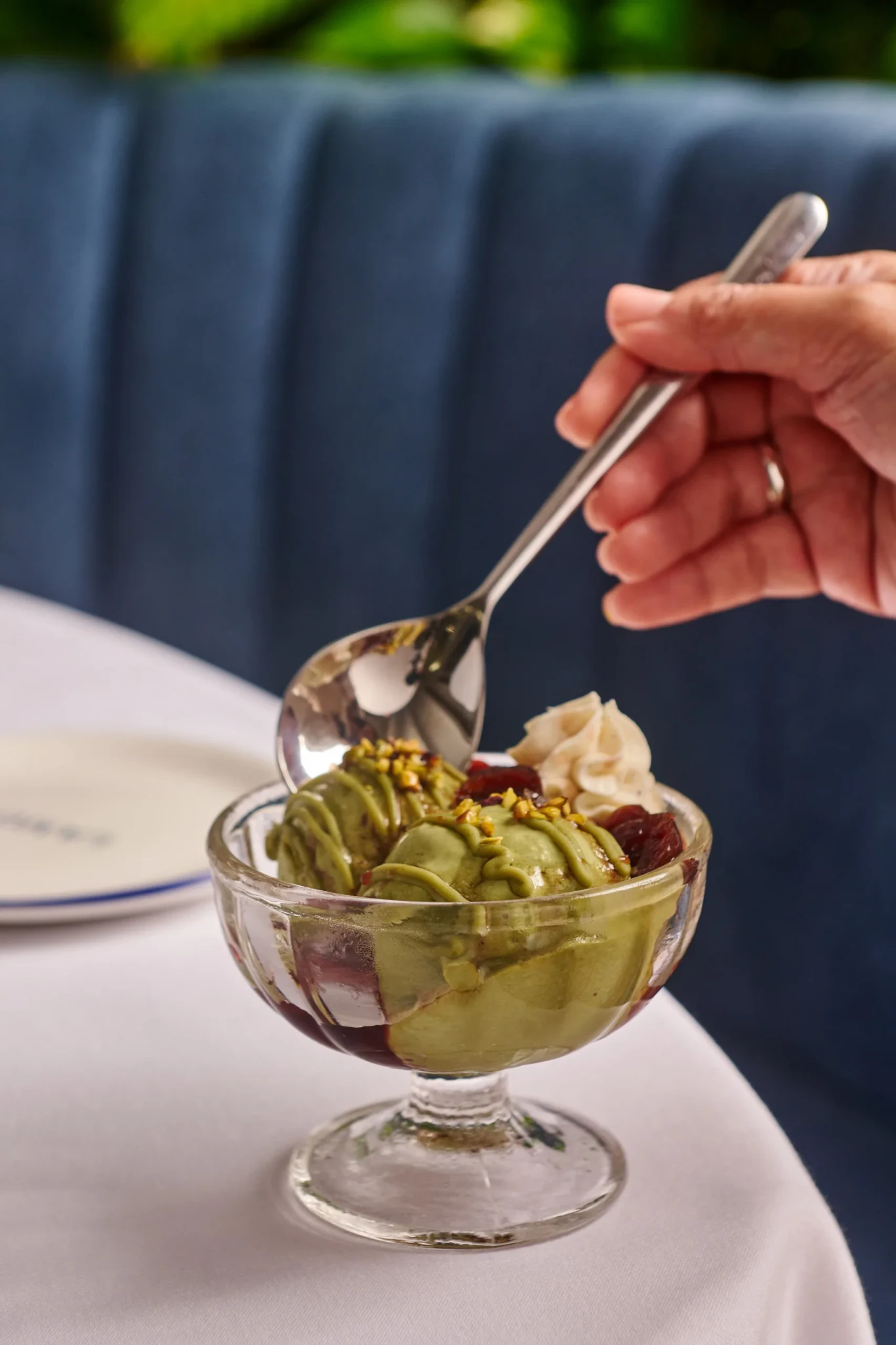 A hand spooning pistachio gelato topped with cherries and chopped pistachios