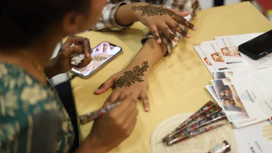 A henna artist applying a floral mehndi design to a visitor's hand at lyf Farrer Park