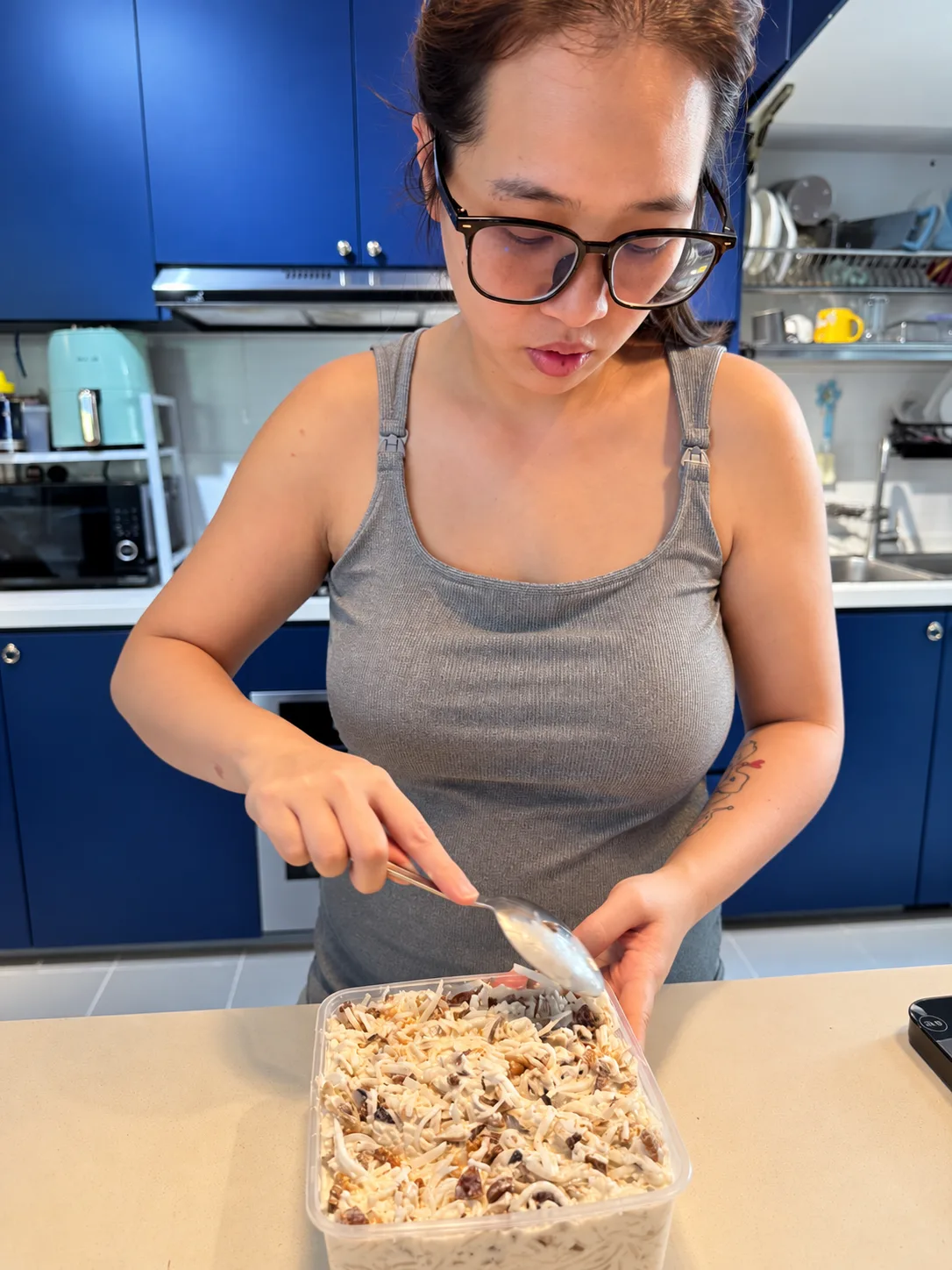 Amelia spoons a topping over a tray of radish cake mixture in her home kitchen.