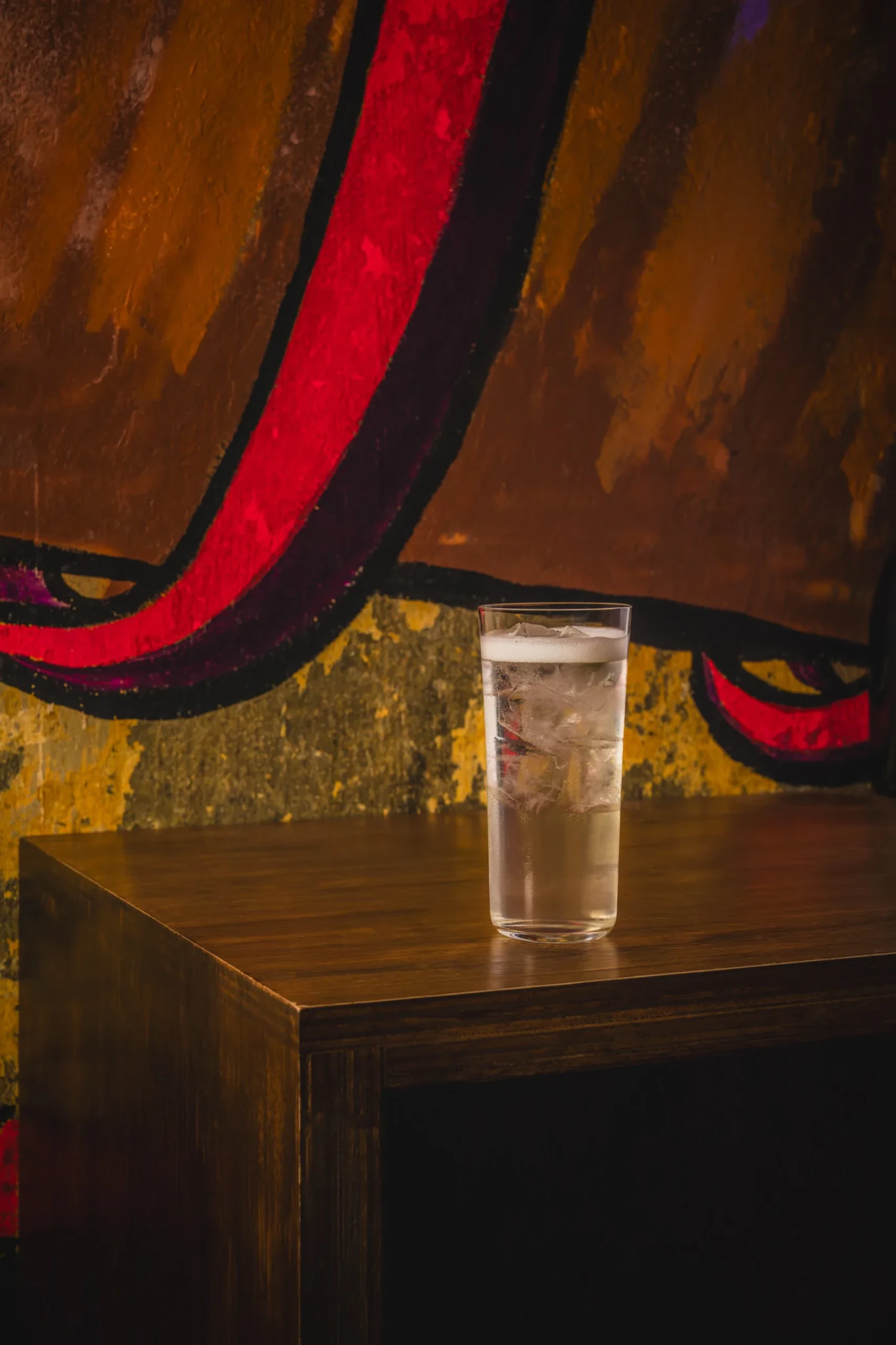 A tall iced drink with a foamy top on a wooden table in front of a colourful mural