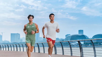 Two runners in adidas running apparel jog along a waterfront promenade with the Singapore skyline and the Esplanade domes behind them