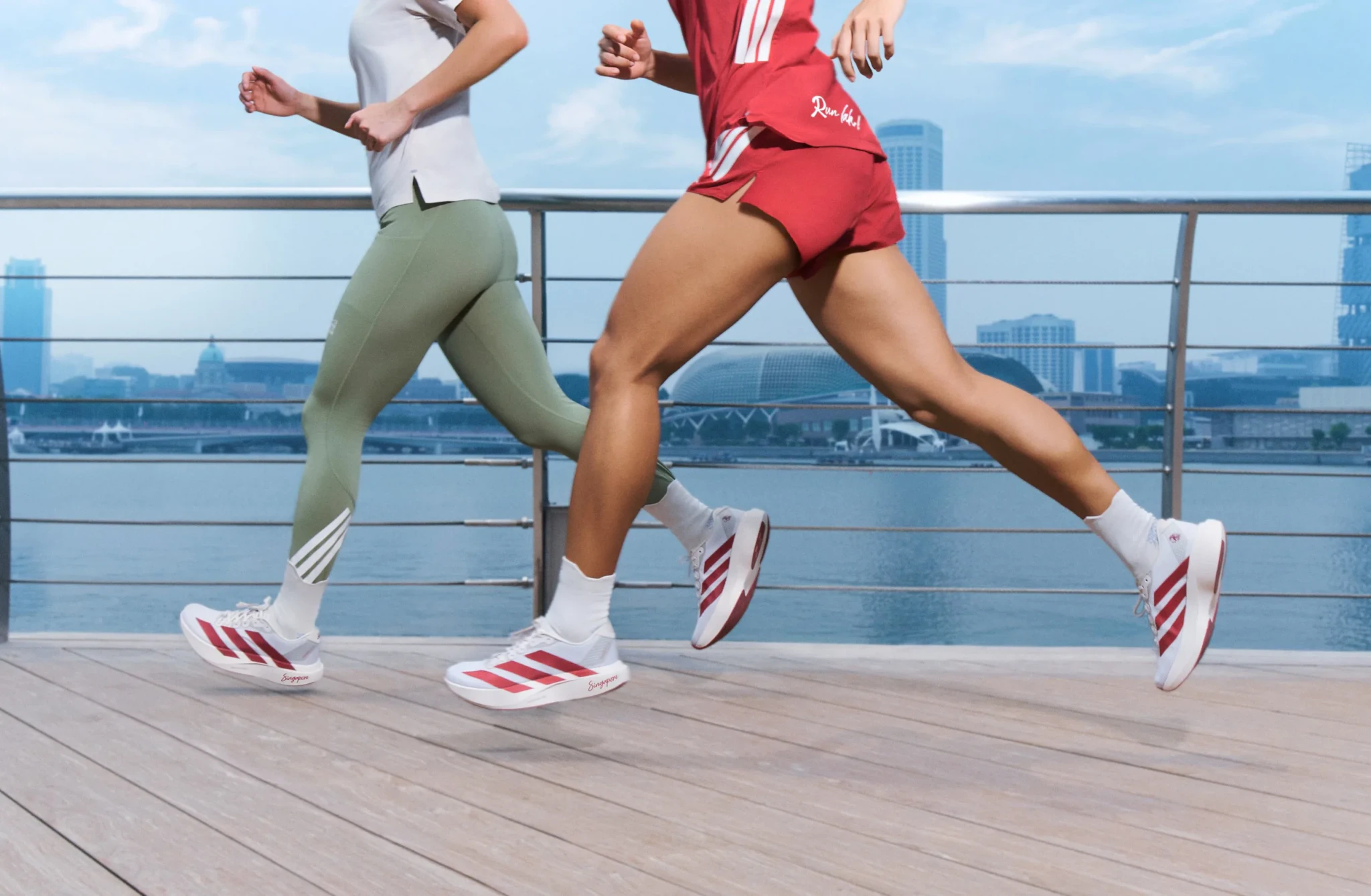 Two runners in adidas running gear and white-and-red ADIZERO Evo SL shoes run along a waterfront promenade