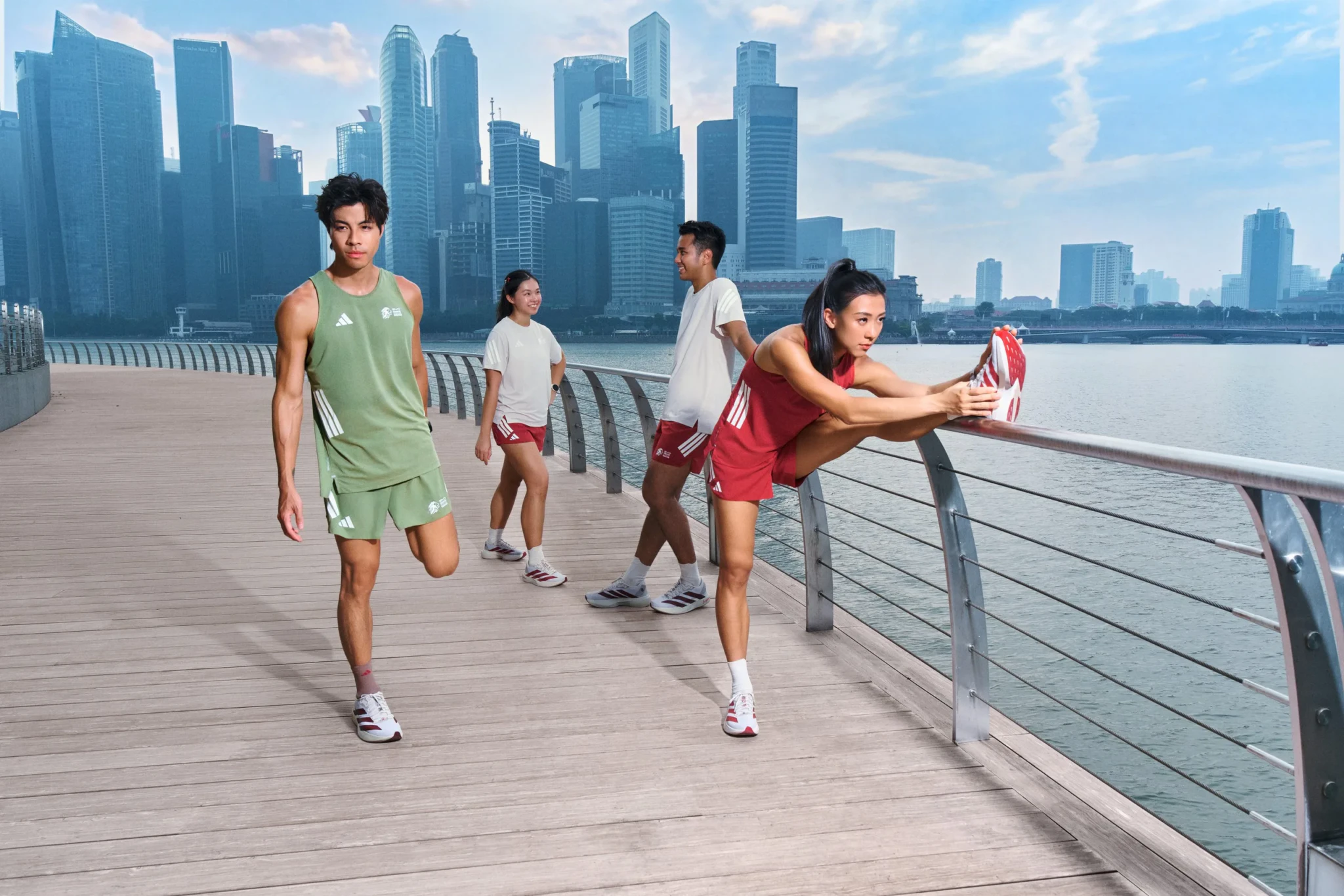 Runners in adidas SGIM26 Capsule Collection apparel stretch along a waterfront boardwalk with the city skyline behind them