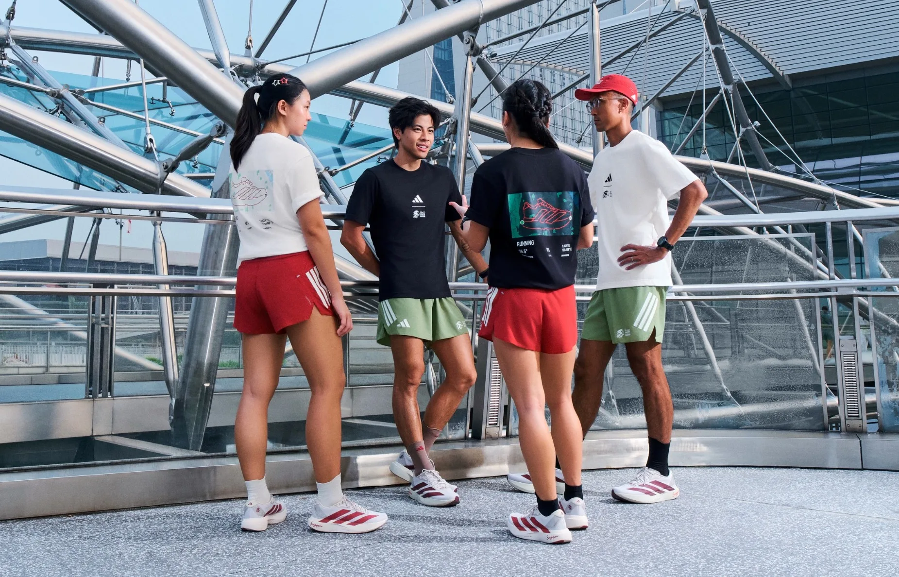 Four runners wearing the adidas SGIM26 capsule collection gather on a glass-and-steel walkway in Singapore