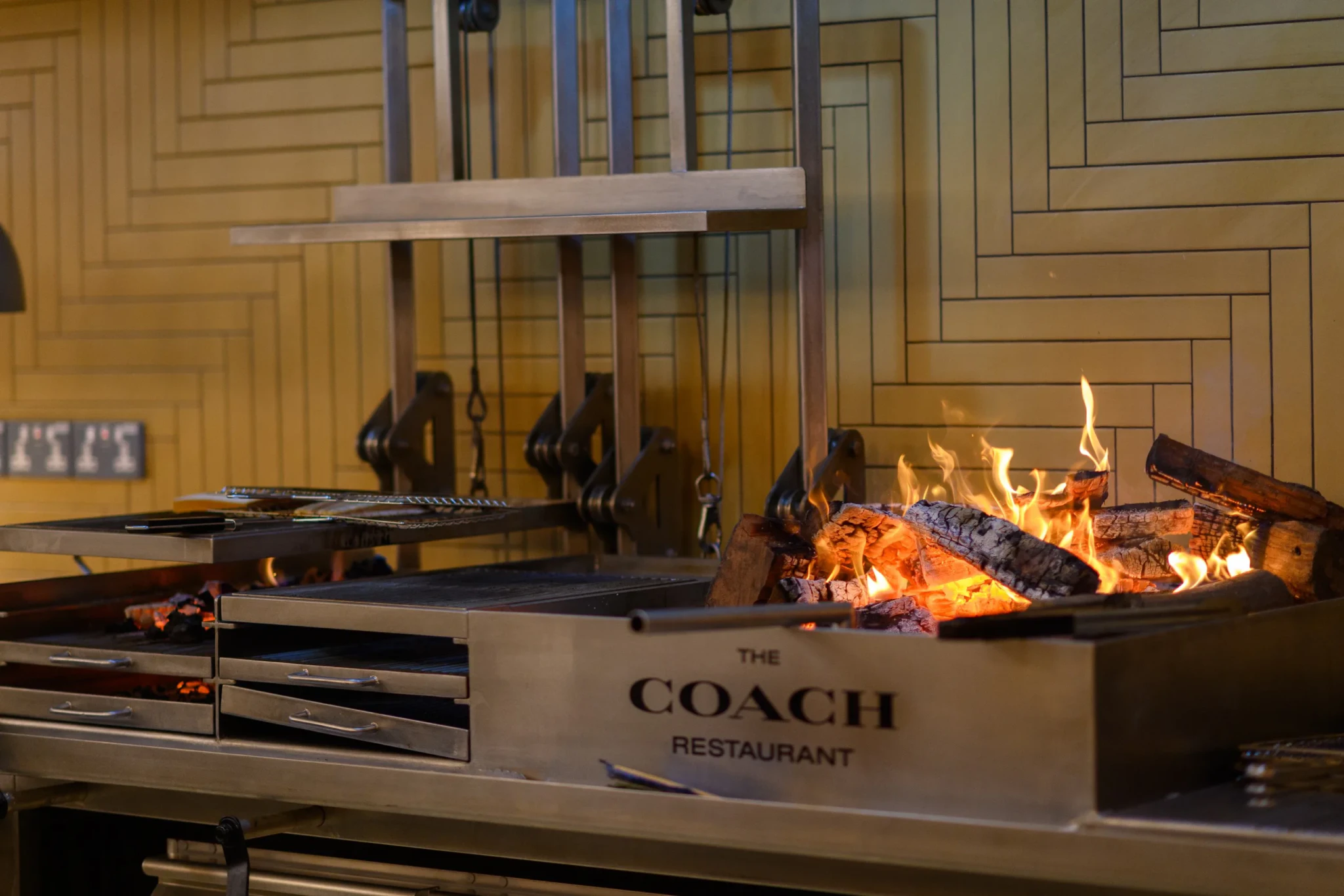 An open woodfire grill with burning logs and a rotating spit at The Coach Restaurant, Jewel Changi Airport