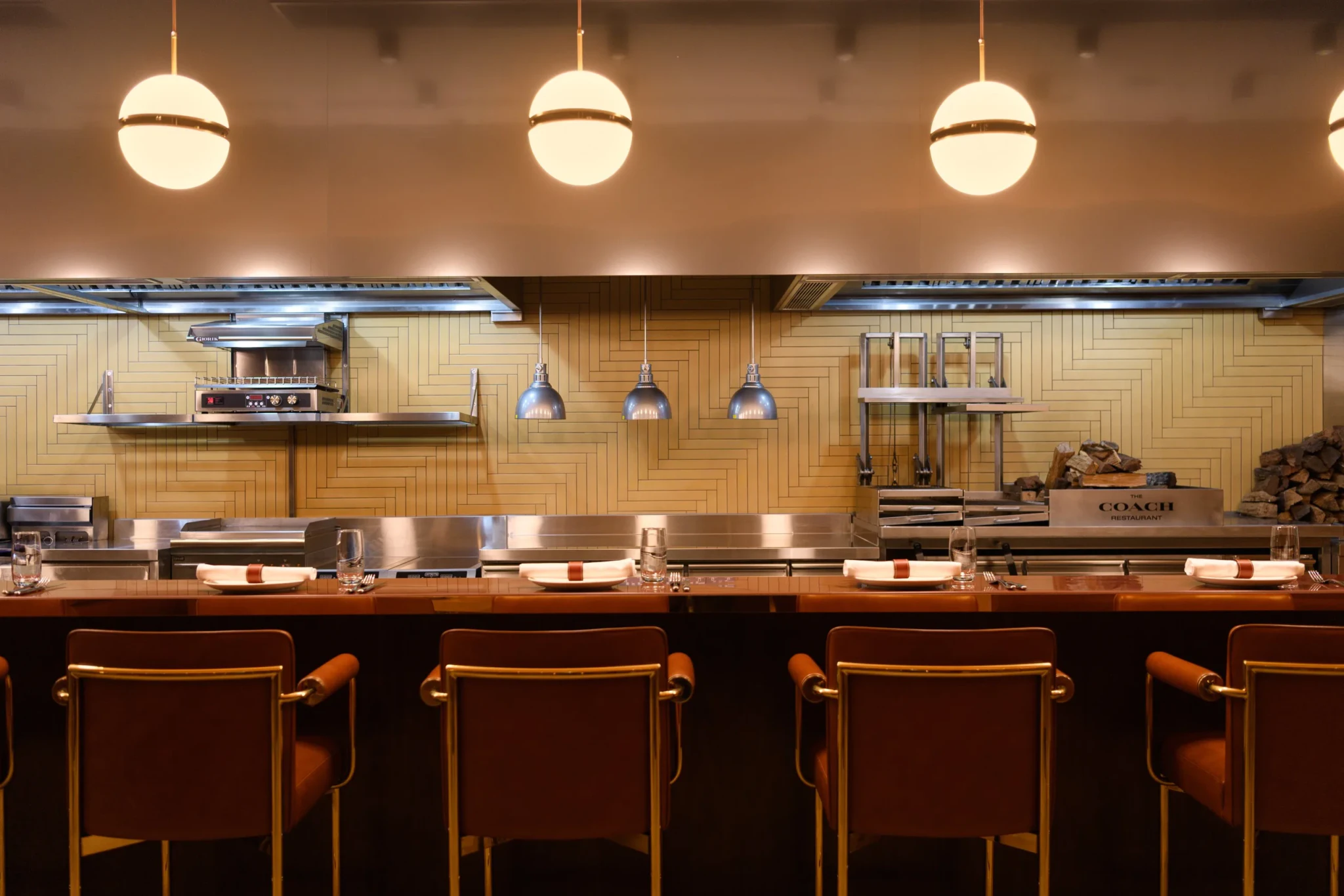 The chef's counter at The Coach Restaurant with linen-wrapped place settings and brown leather stools facing the open kitchen
