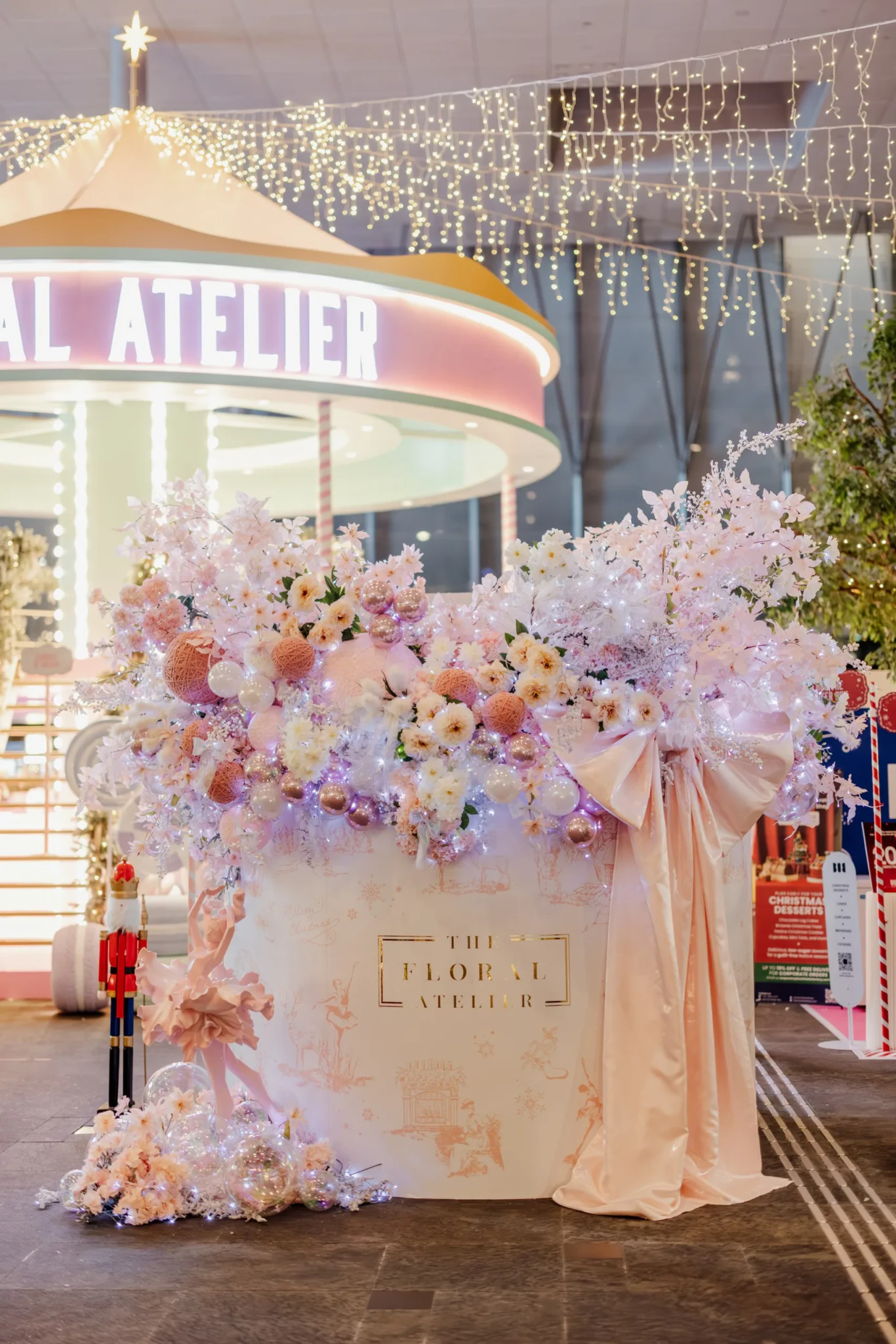 A pink-and-white floral arrangement with a large satin bow and a nutcracker figure beneath festive string lights