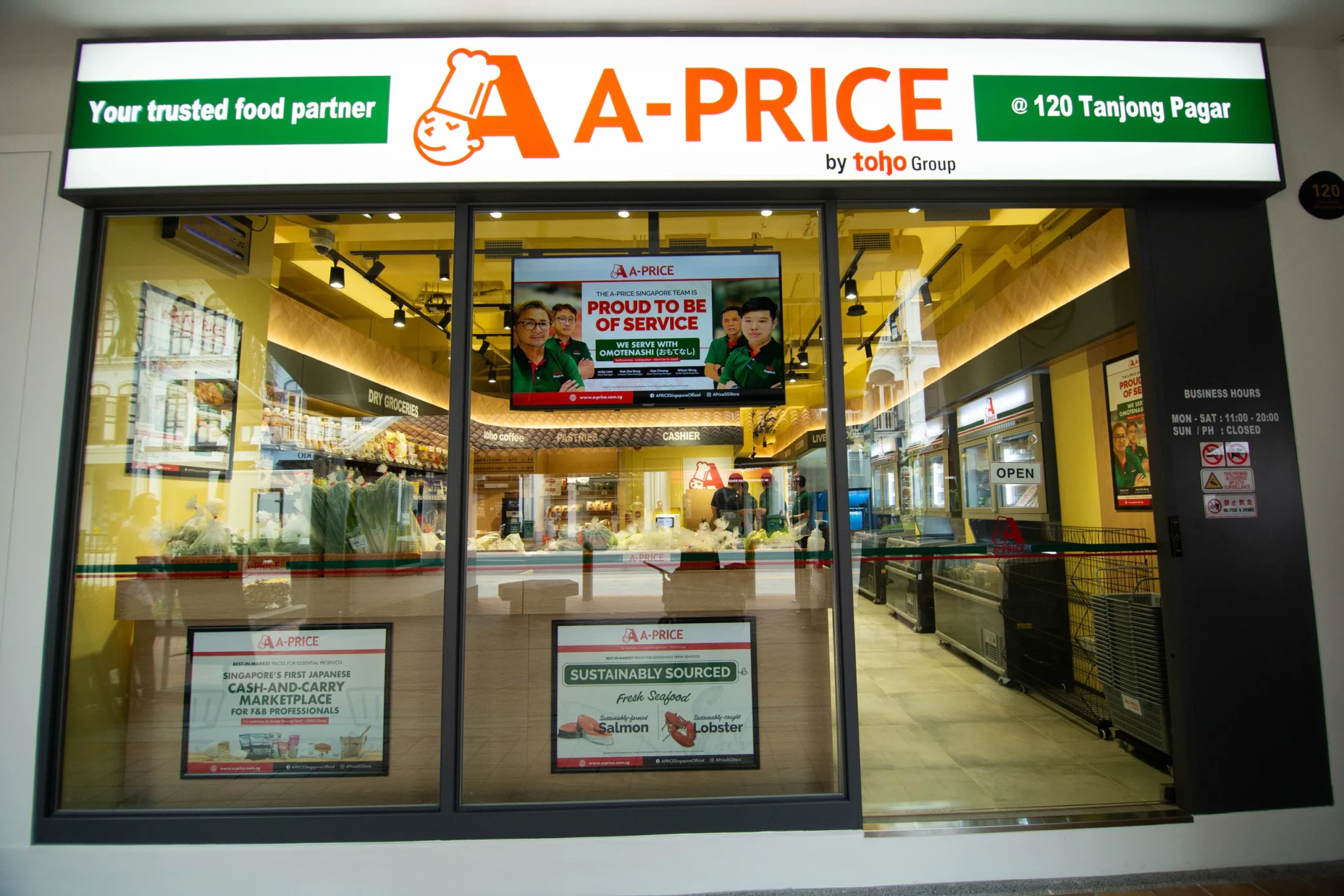 A-PRICE store front at 120 Tanjong Pagar with a screen showing staff and 'Proud to be of service' slogan