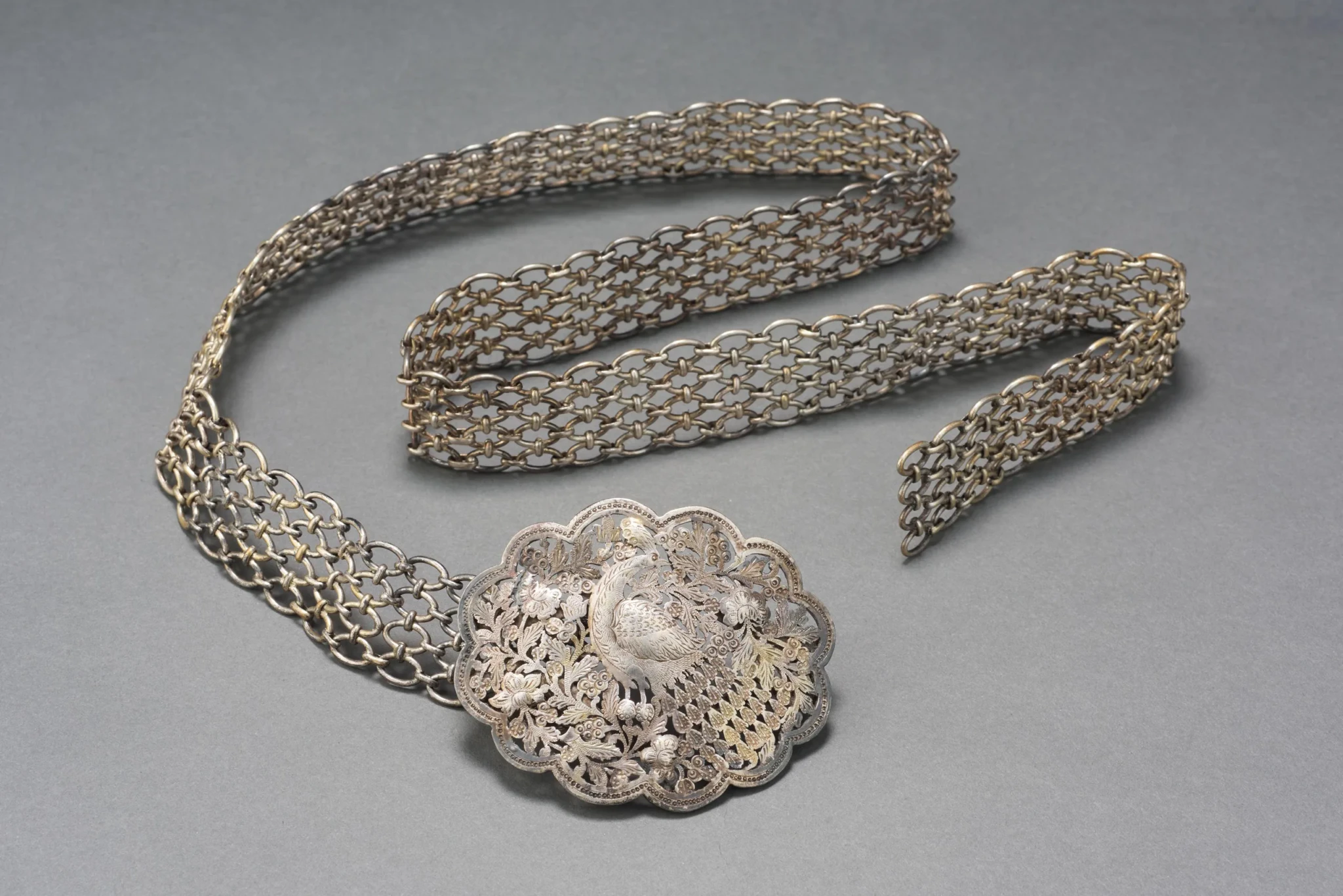 A silver filigree belt with a scalloped openwork buckle decorated with a peacock and floral motifs