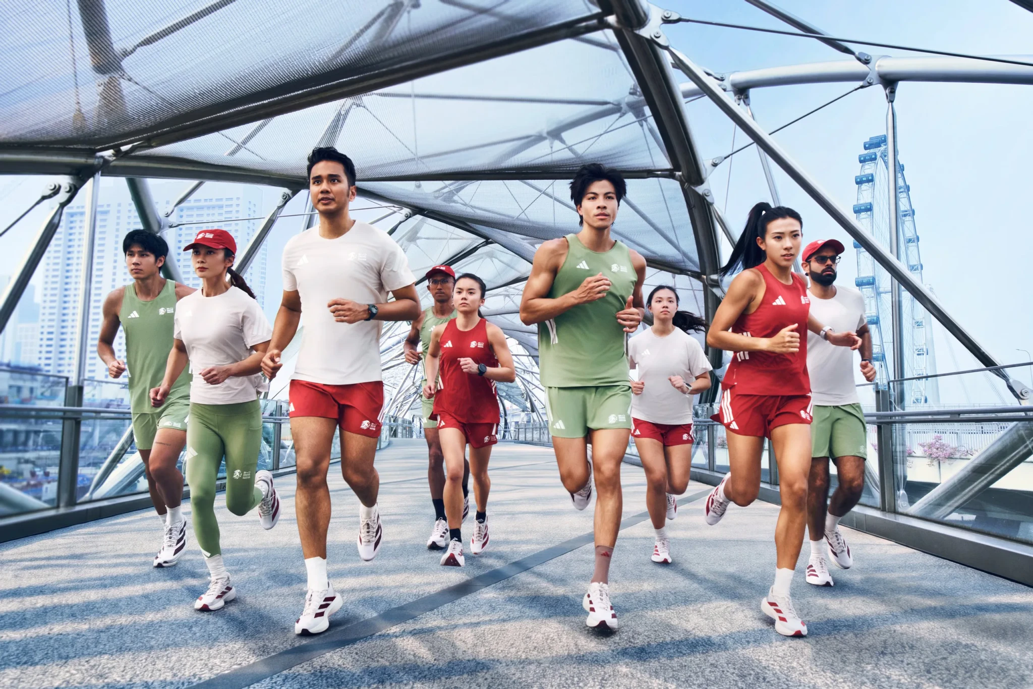 Six runners in green sleeveless tops and red running sets crossing a glass-and-steel footbridge with the Singapore Flyer behind them