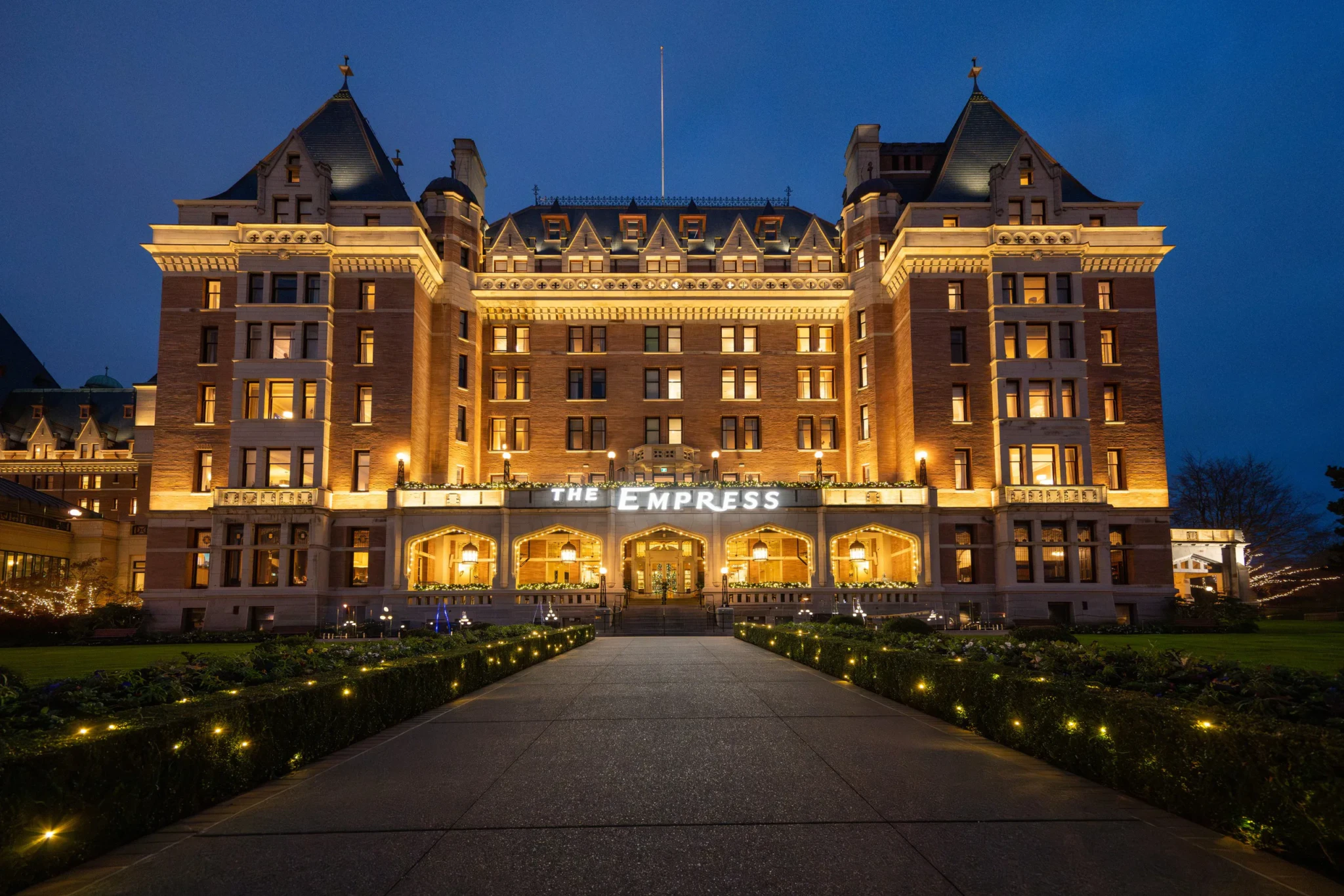 Illuminated brick Fairmont Empress hotel facade at dusk with festive lights lining the front pathway