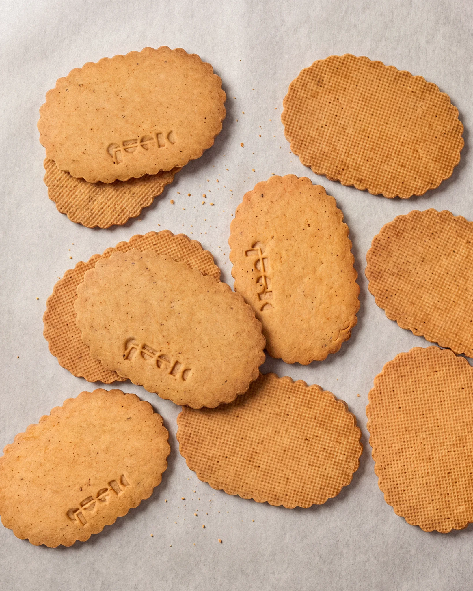 Scalloped oval brown butter hazelnut cookies with stamped and grid-patterned tops scattered on parchment