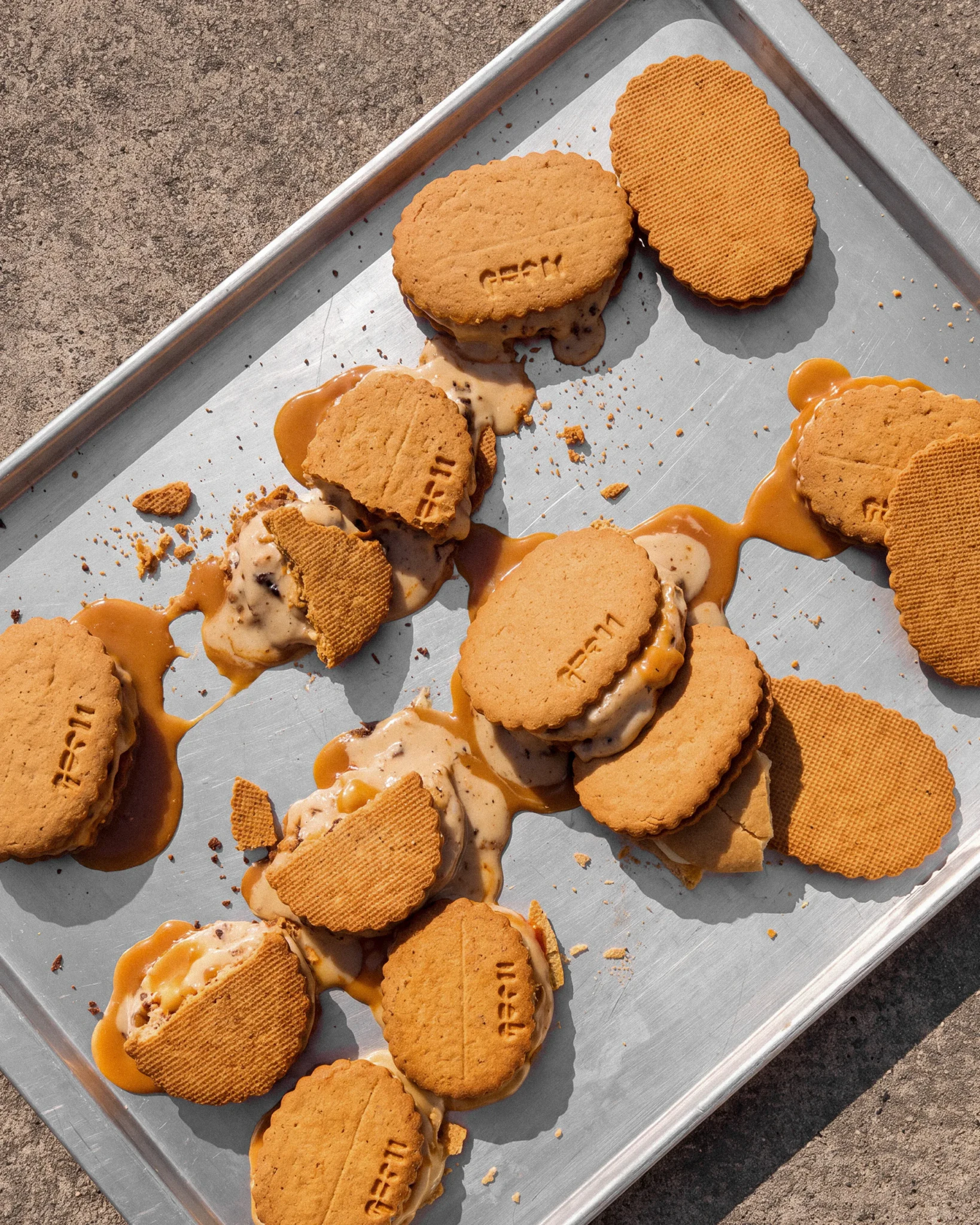 Broken ice cream sandwiches with melting caramel-flecked gelato spilling across a metal baking tray