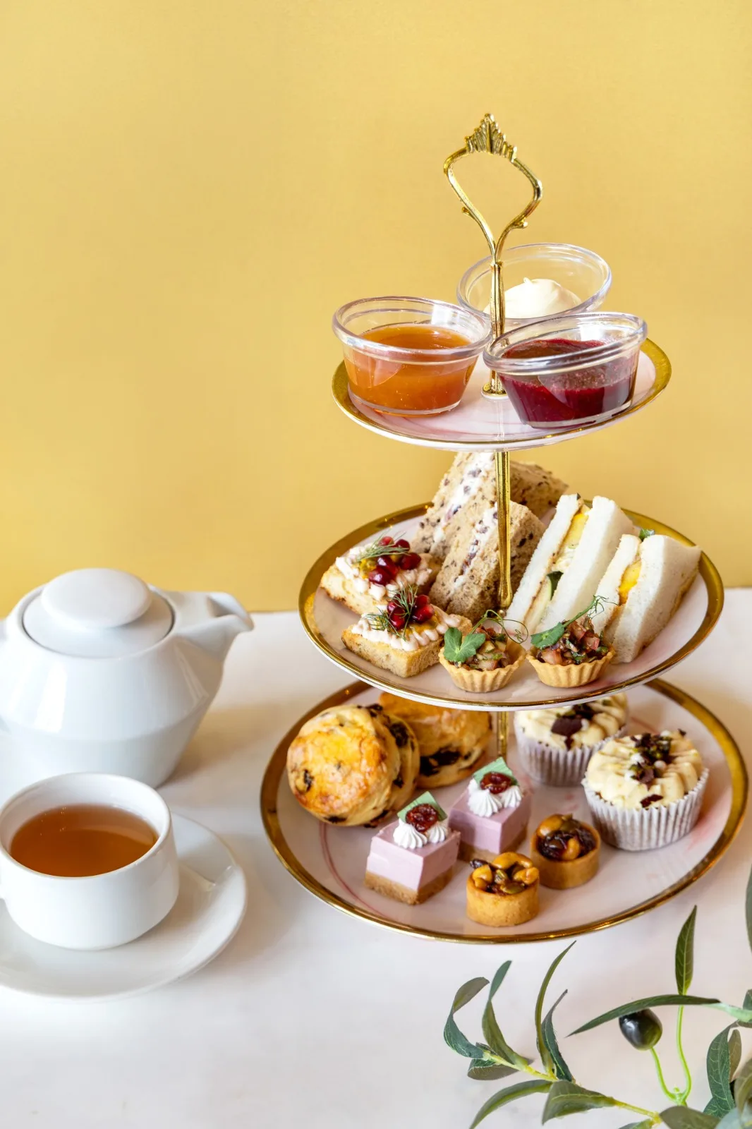 A tiered afternoon tea stand with sweet and savoury bites, jams and preserves, and a pot of tea