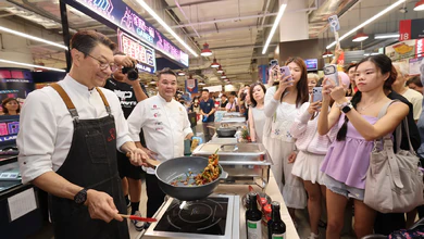 Chef Eric Teo demonstrates wok cooking at Xtra Lab in FairPrice Xtra Ang Mo Kio Hub as shoppers watch and take photos