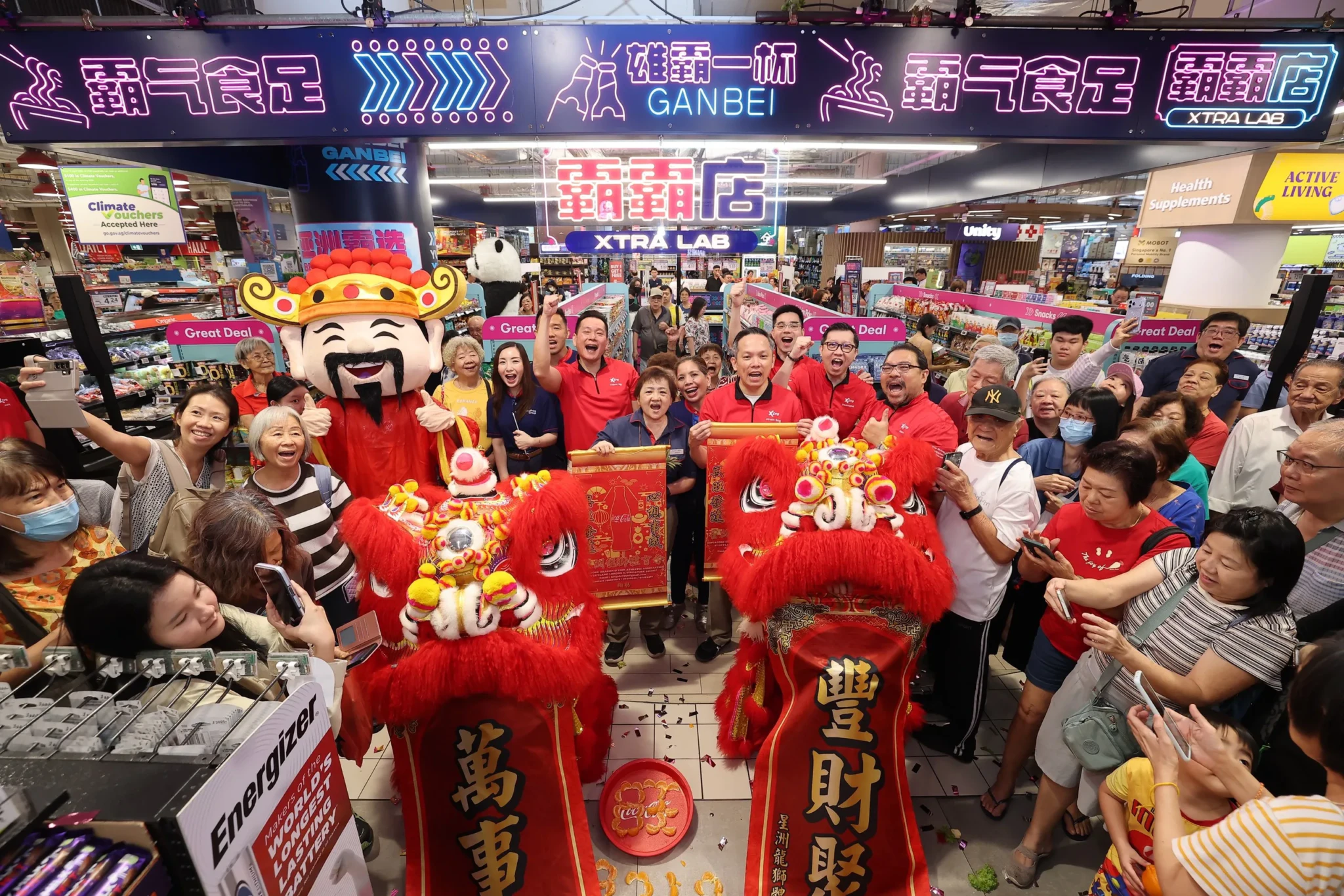 Shoppers and staff in red crowd around a lion dance and God of Wealth mascot at the Xtra Lab launch at FairPrice Xtra AMK Hub