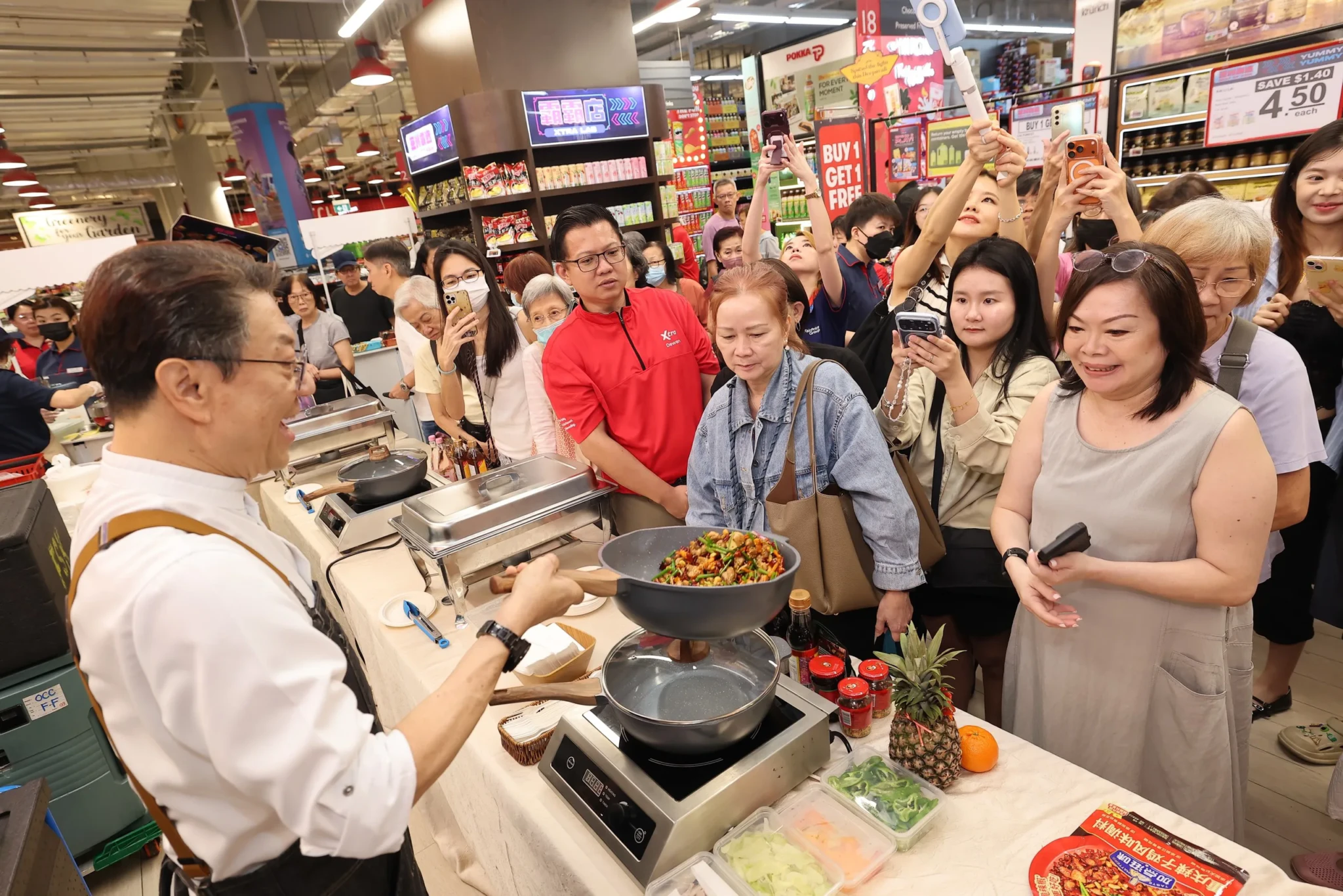 Chef Eric Teo leads a live cooking demonstration at FairPrice Xtra as shoppers crowd around the stir-fry station to watch.