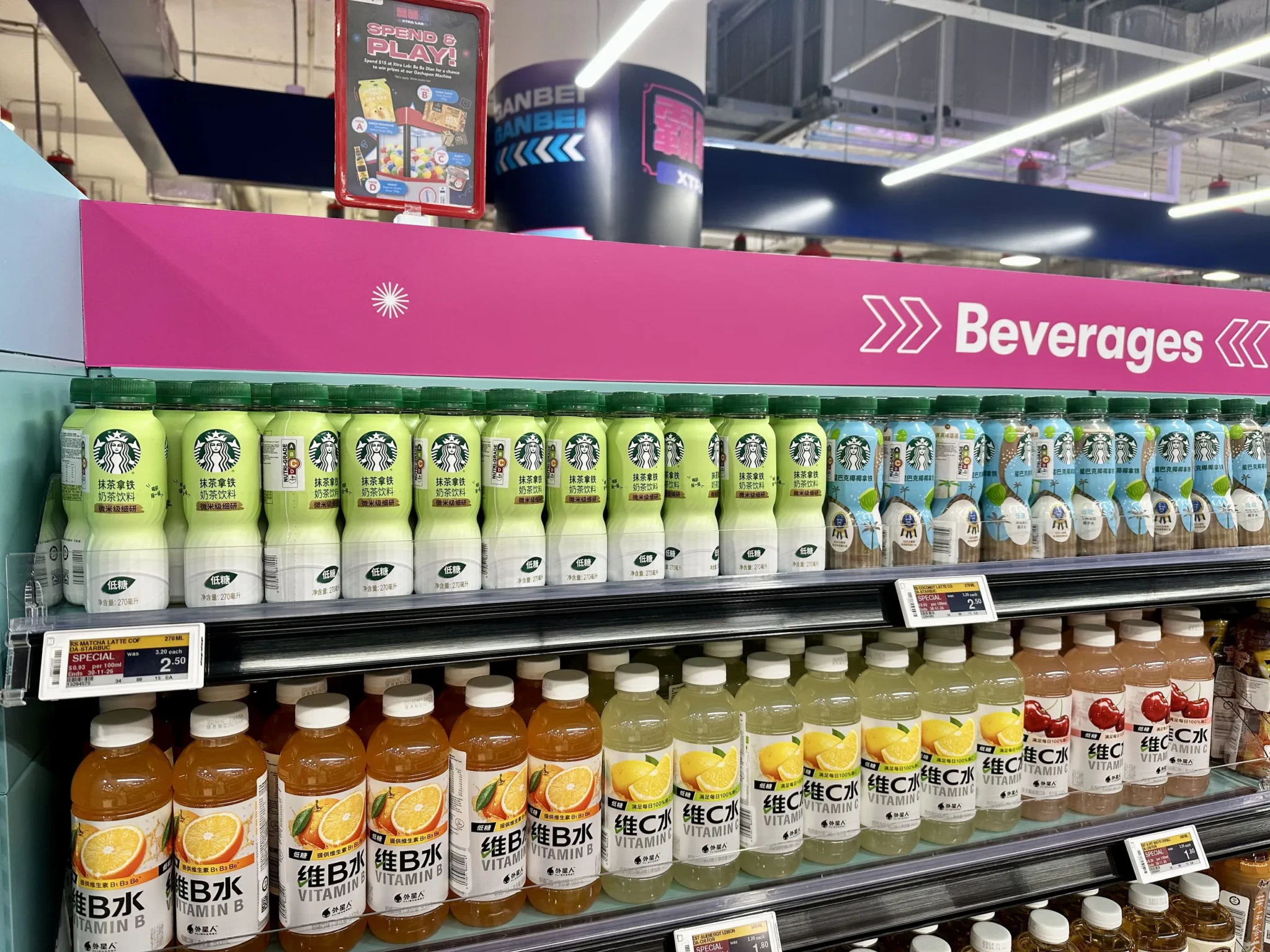 Assortment of beverages on display at FairPrice Xtra Ba Ba Dian, including Starbucks matcha latte and coconut latte bottles and Vitamin B and Vitamin C drinks o